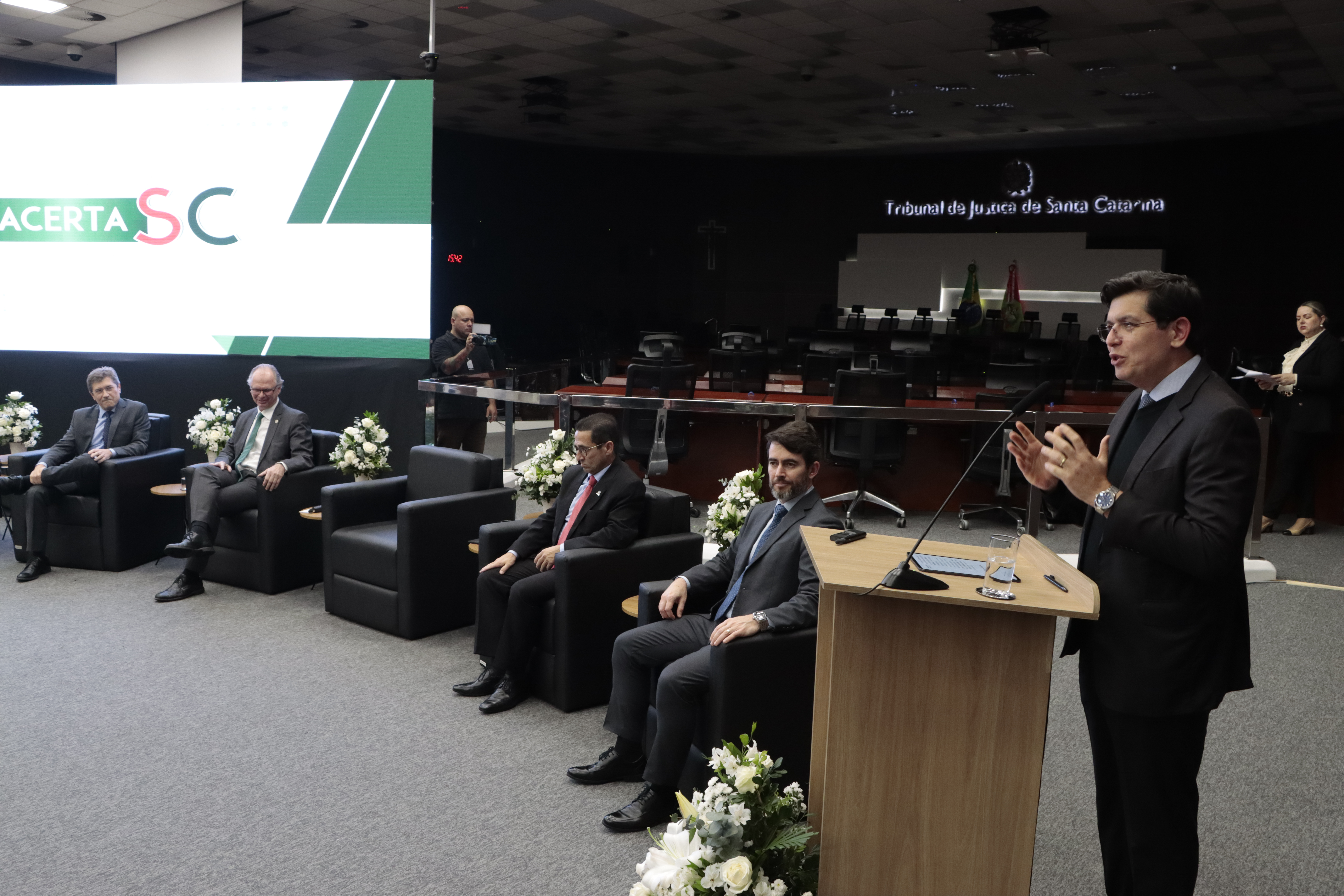 Foto horizontal do conselheiro do CNJ Marcello Silva falando ao púlpito. É um homem branco, de cabelos escuros. Veste terno escuro. Ao seu lado, há outras autoridades sentadas em poltronas.