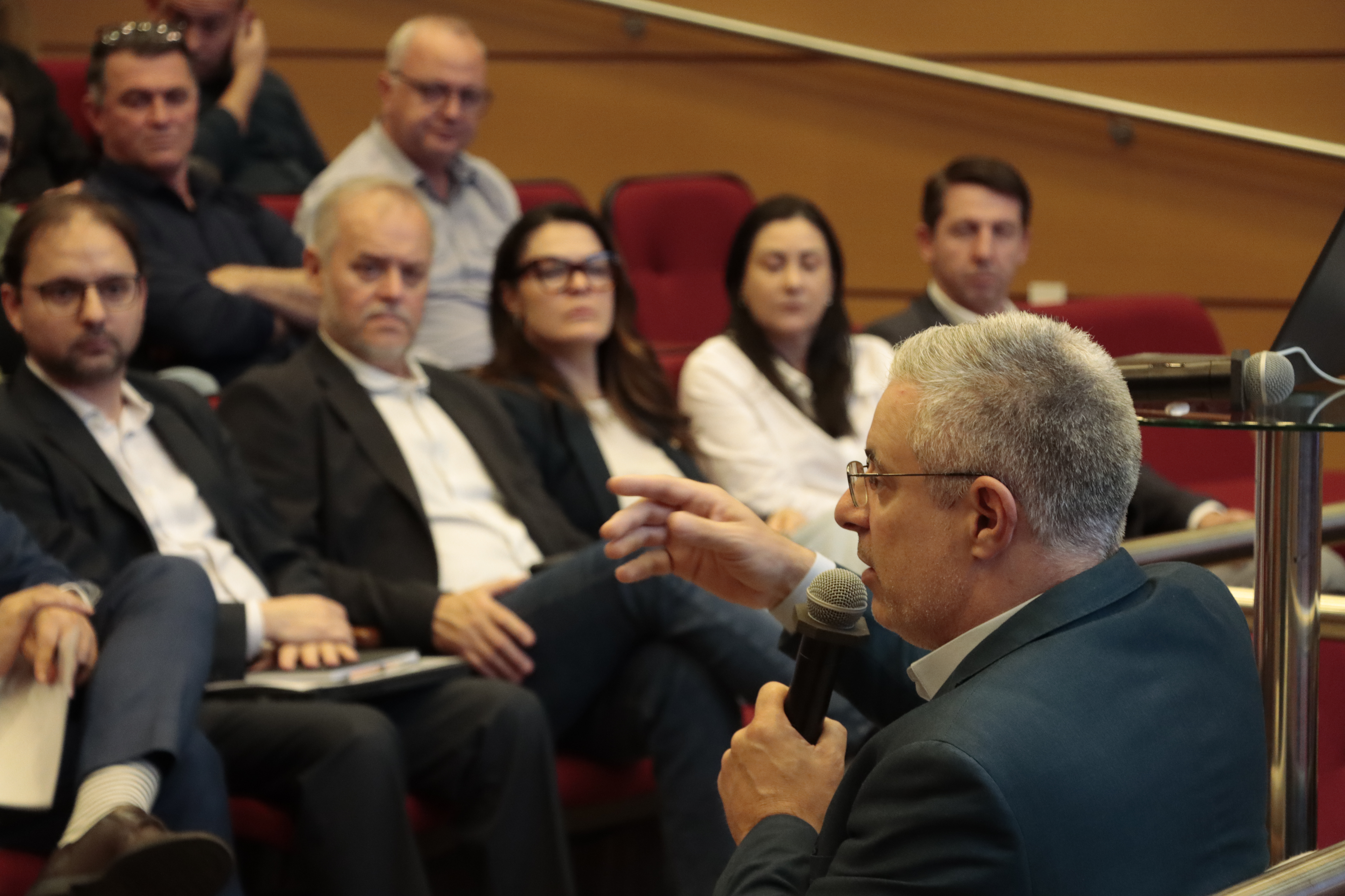 Foto horizontal que mostra o conselheiro Gerson Sicca, de costas, falando ao microfone no auditório do TCE. À sua frente, a plateia participante.