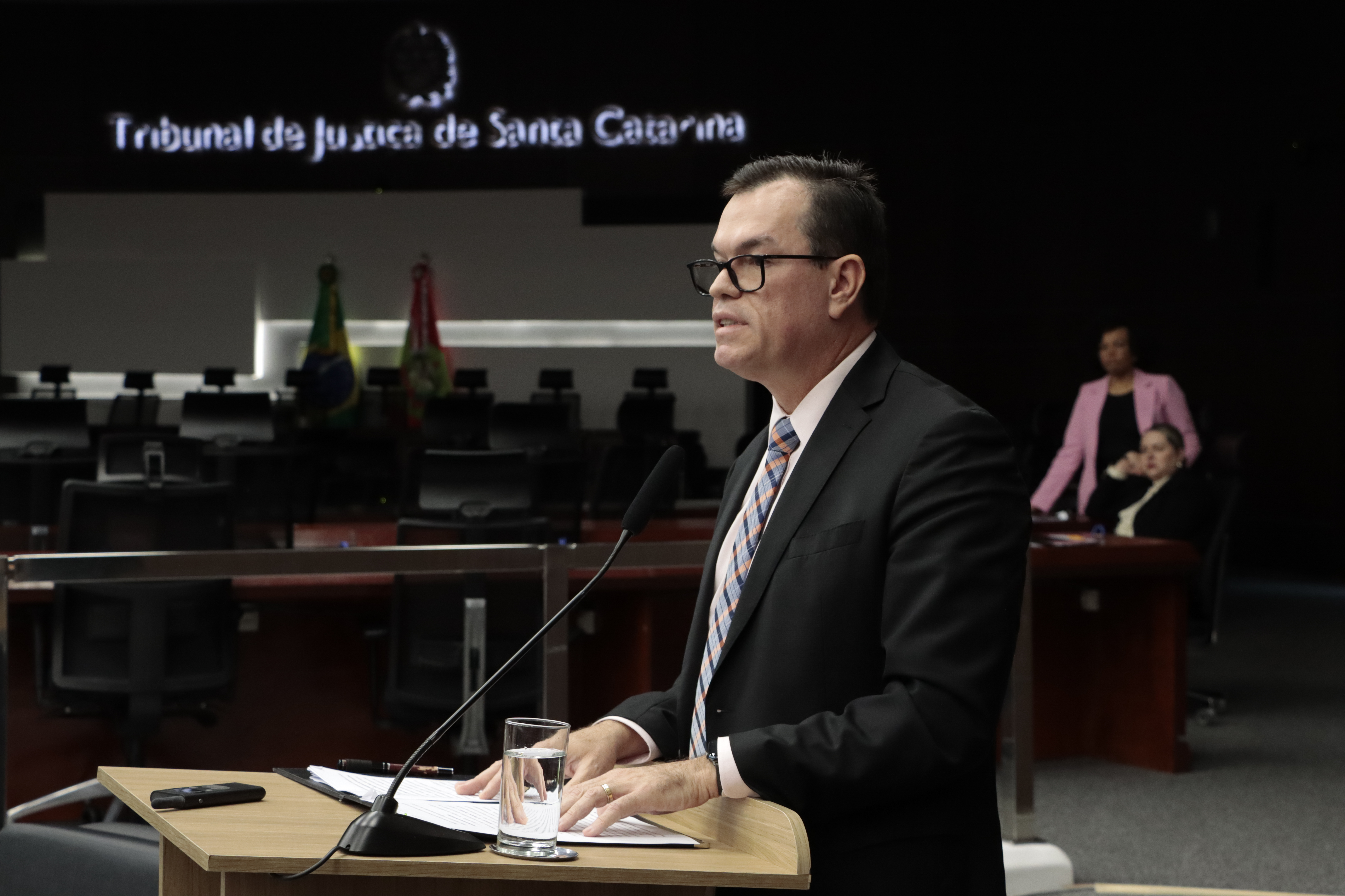 Foto horizontal do conselheiro Adircélio falando ao púlpito, no auditório. É um homem branco, de cabelos escuros. Veste terno escuro e usa óculos de grau.  