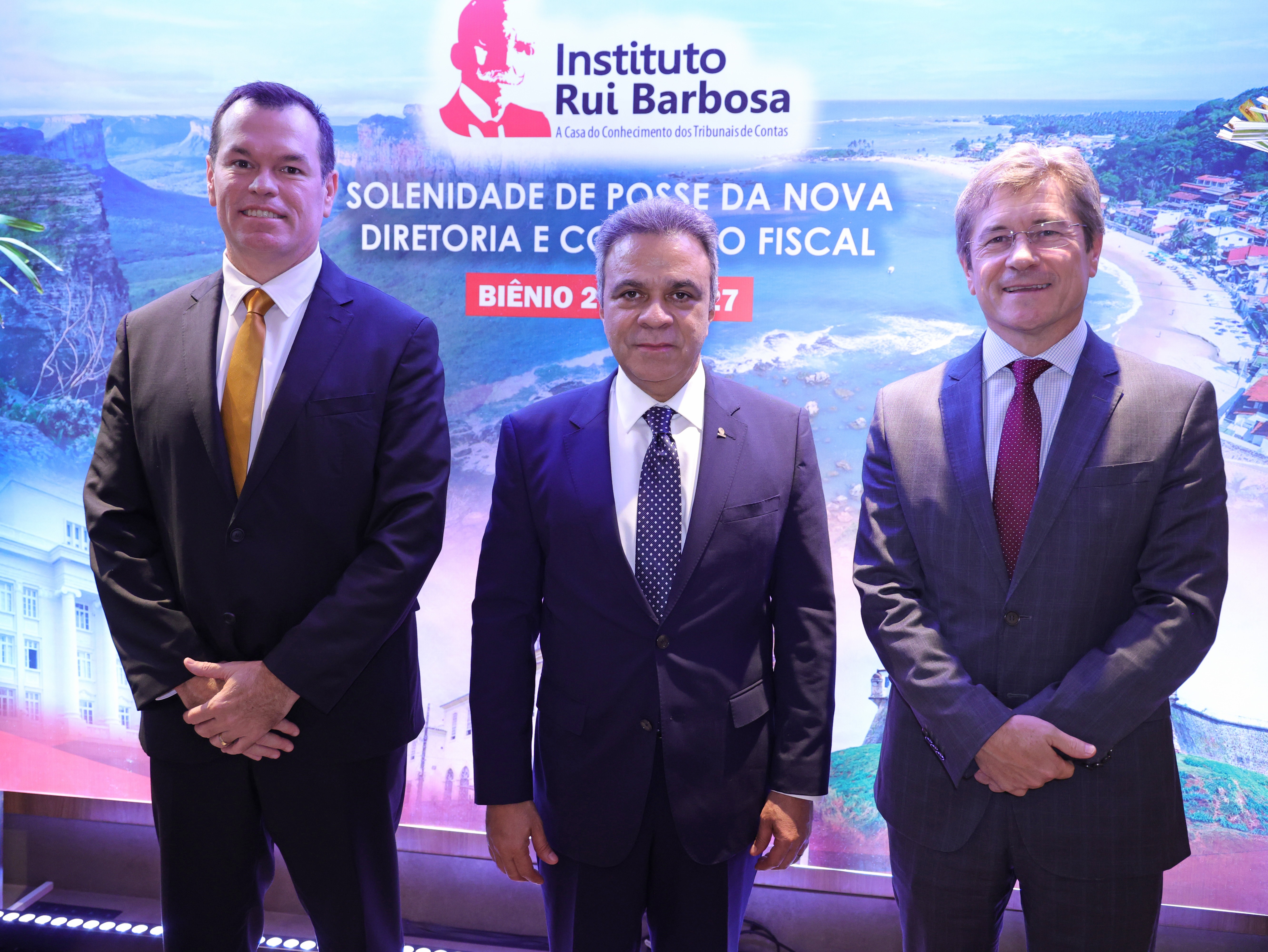 Banner horizontal com foto dos conselheiros Adircélio Ferreira Júnior, Edilson Silva e José Nei Ascari. Eles estão lado a lado, em pé, em frente a um backdrop com logo do IRB. Ambos vestem terno e gravata e sorriem. 