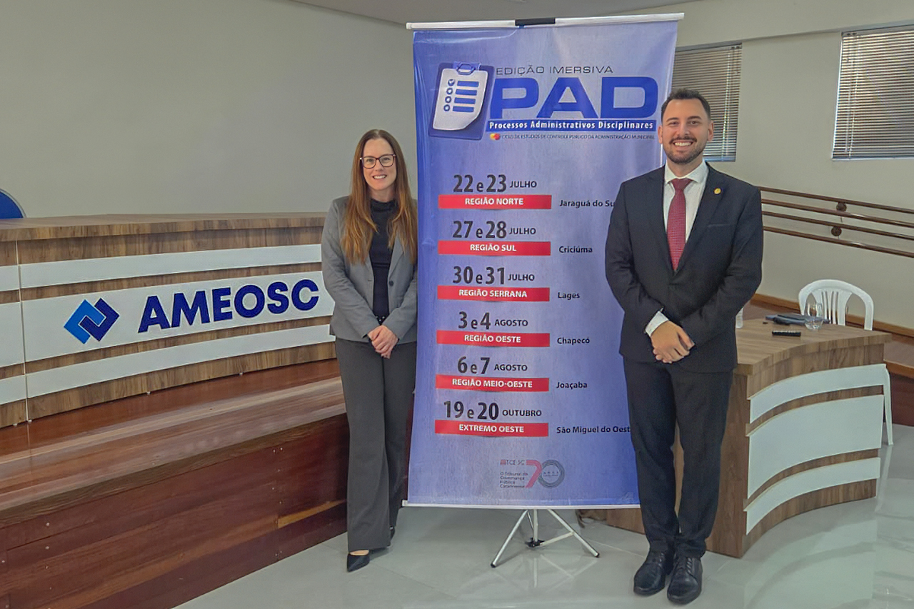 Foto horizontal da etapa de São Miguel do Oeste. À direita, o servidor do TCE/SC Geovane Cardozo, e à esquerda a servidora Vivian Savedra. Entre eles, o banner vertical do Ciclo - edição imersiva do PAD