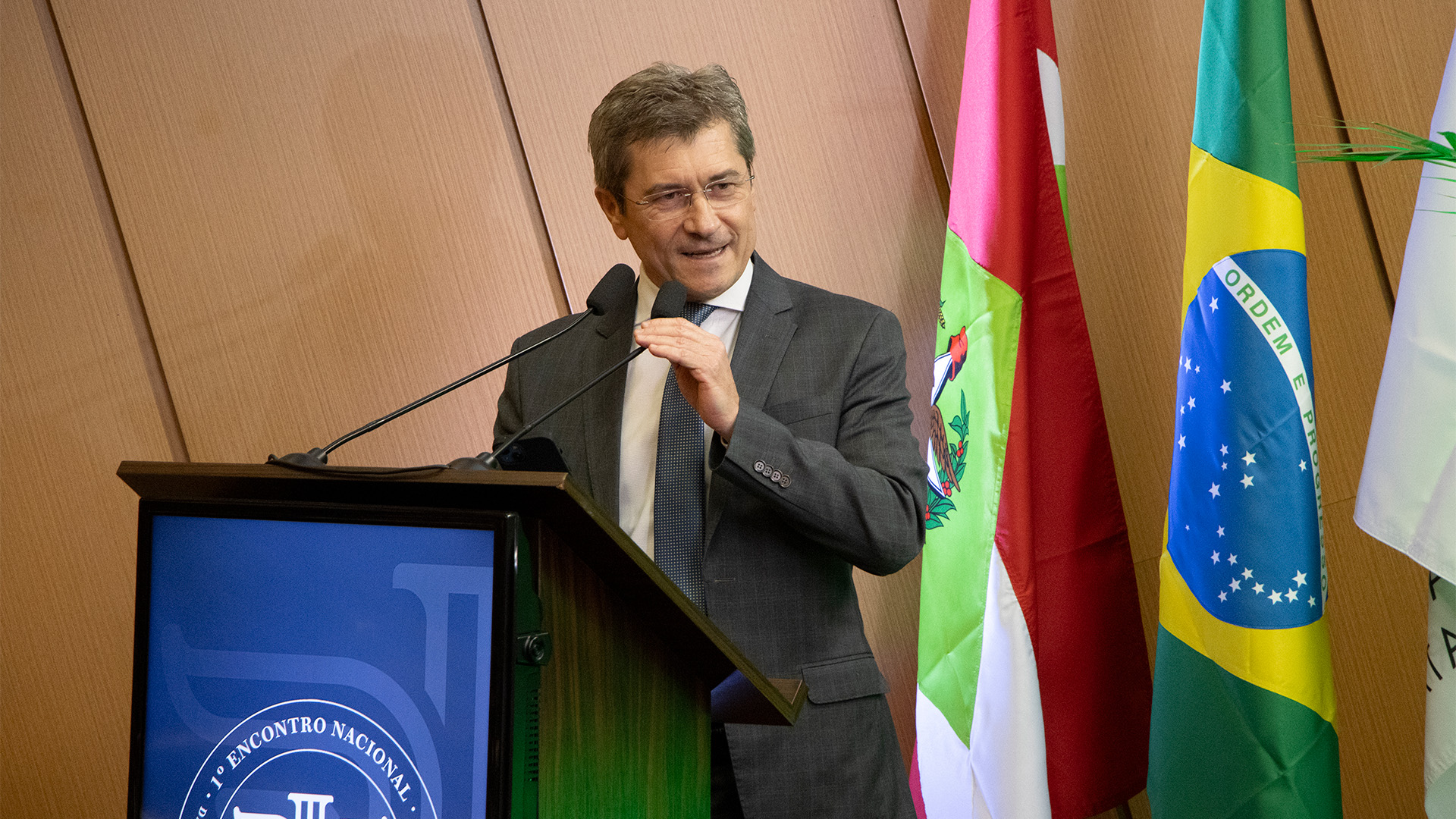 Foto do conselheiro José Nei Ascari falando no púlpito do auditório do TCE/SC, durante o Enapac. É um homem branco, de cabelos grisalhos. Veste terno e gravata e olha para a direita.