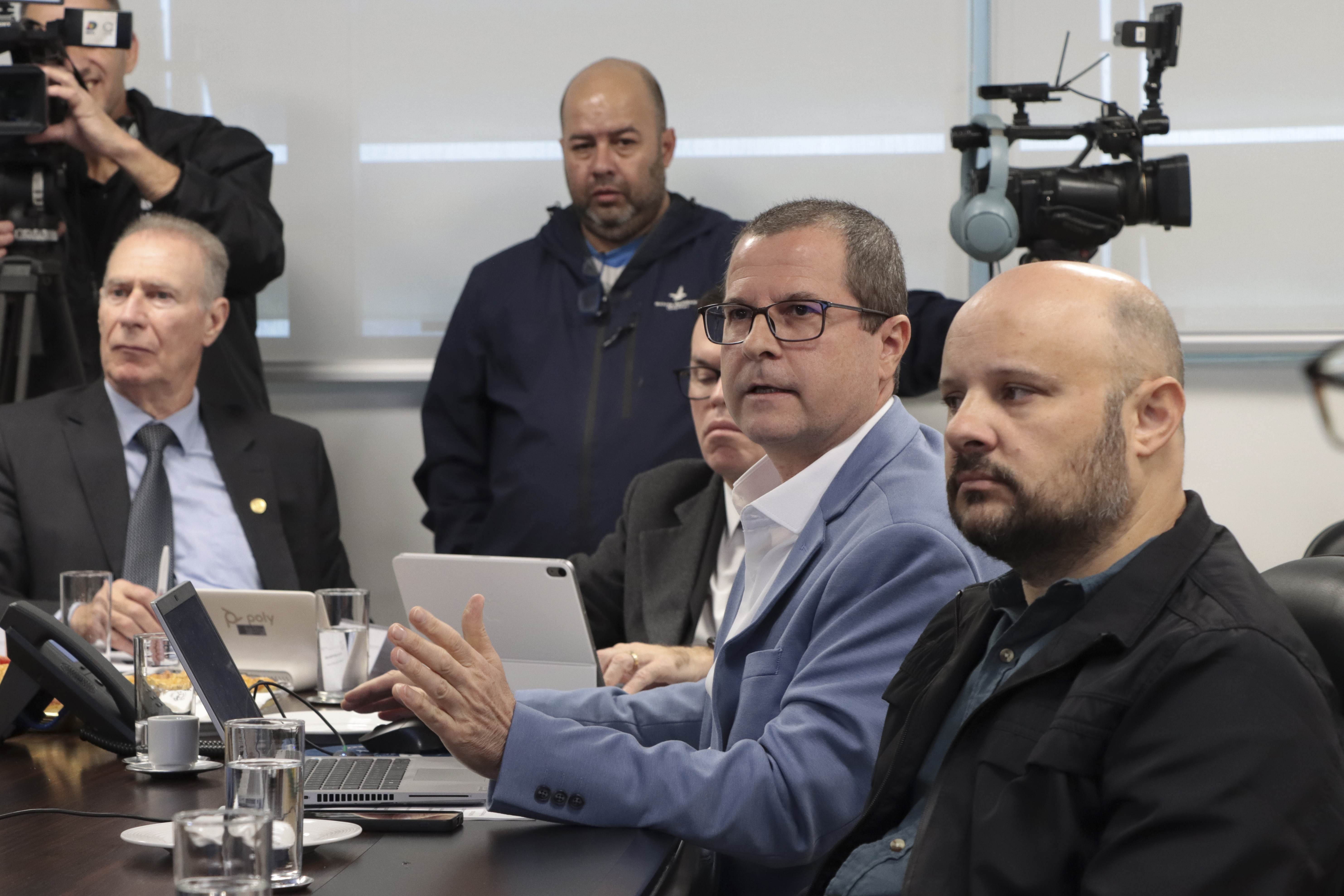 Foto horizontal do diretor Nilsom Zanatto falando aos demais durante reunião. Ele está sentado diante da mesa, ao lado dos demais participantes. Entre eles, o presidente Herneus.
