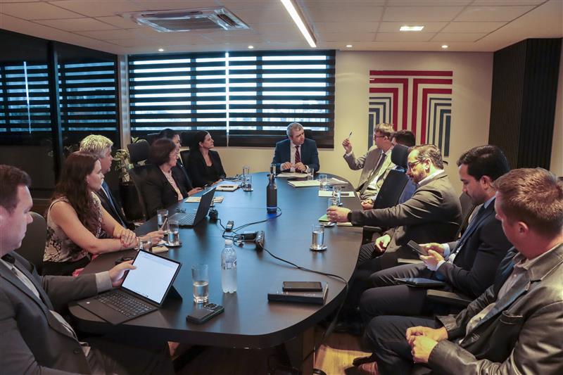 Imagem horizontal de todos os participantes da reunião da mesa de consensualismo. Há várias pessoas sentadas lado a lado, enquanto conversam, em uma sala do TCE/SC. Na ponta, o coordenador da mesa, auditor Márcio Medeiros.
