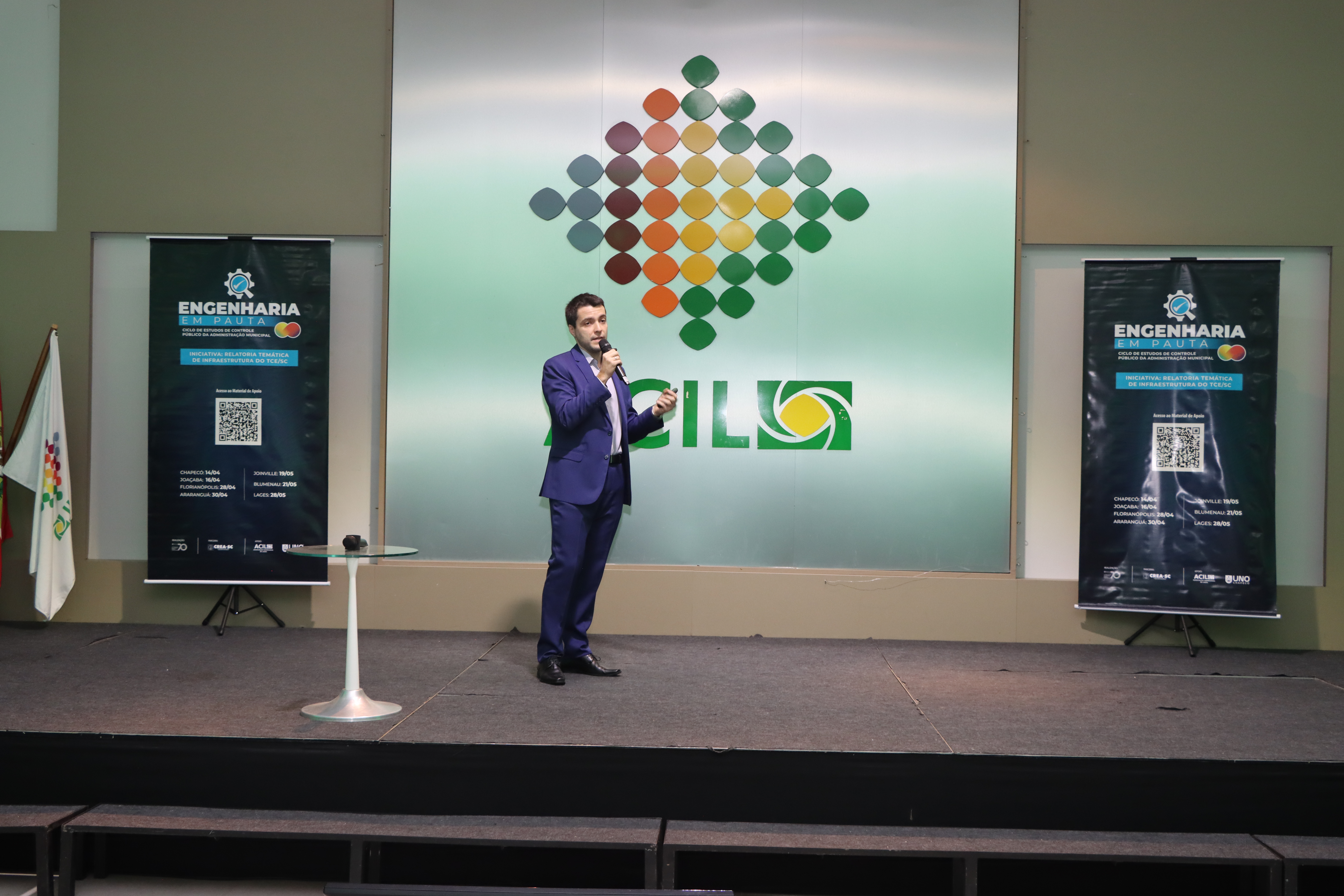 Foto do auditor fiscal de controle externo da DLC Douglas Ancelmo no palco palestrando.