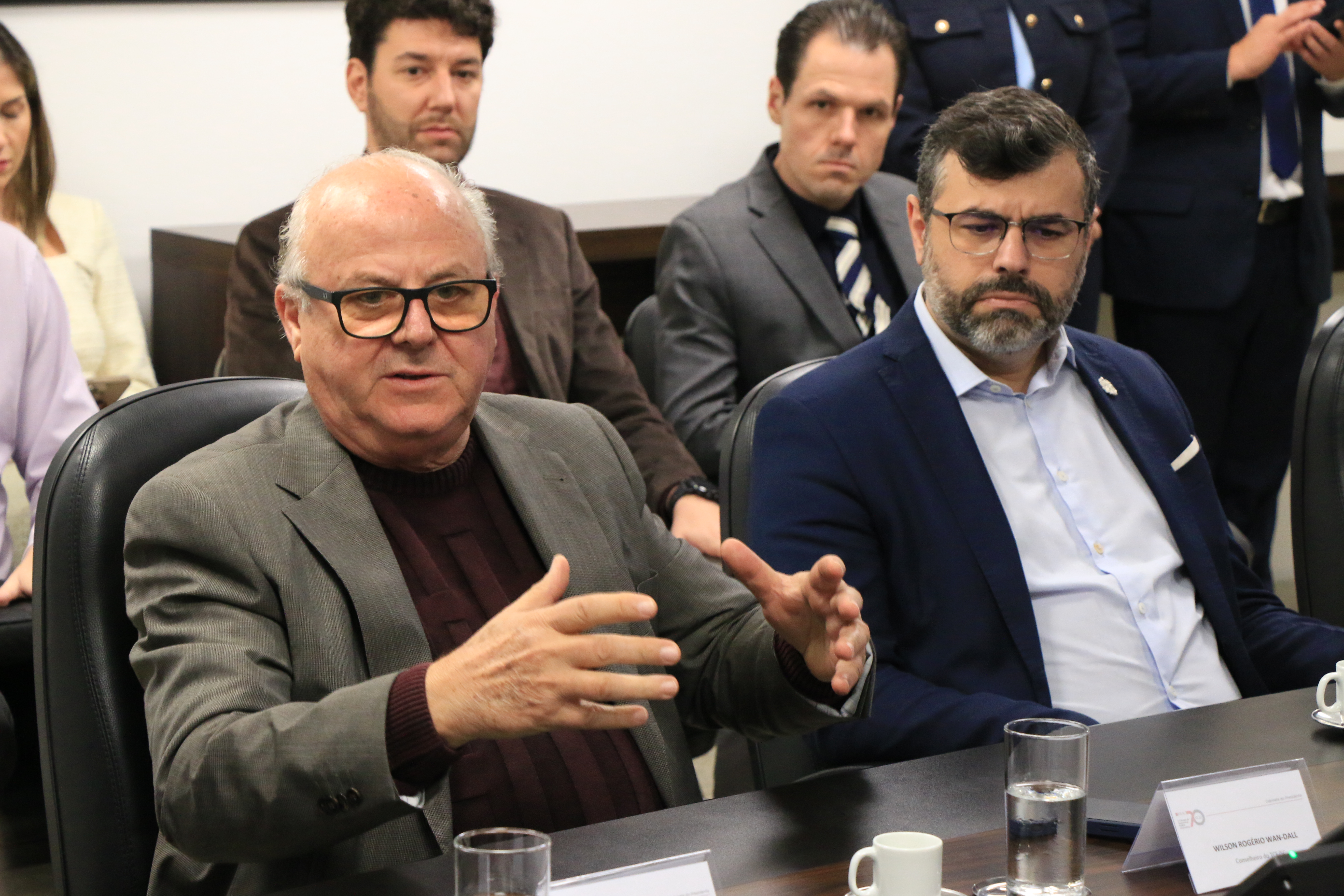 Foto horizontal do conselheiro Wilson Wan-Dall falando aos demais durante a reunião. Ele está sentado diante da mesa, ao lado de outros participantes. Gesticula enquanto fala. 