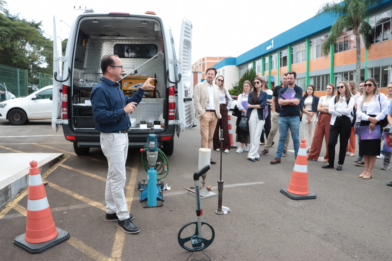 Foto externa com a unidade móvel do Laboratório de Obras Rodoviárias. Em primeiro plano, o auditor do TCE/SC Rodrigo Glória explica para os participantes do evento  as funcionalidades do laboratório.