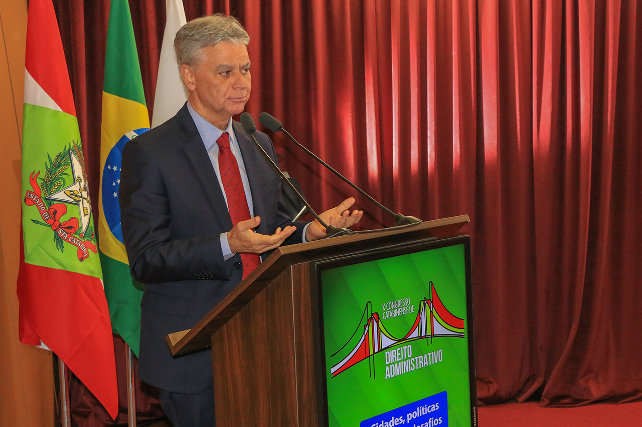 Foto horizontal do desembargador Rodrigo Collaço discursando no púlpito do auditório bordô do TCE/SC. Ele é um homem branco, de cabelos grisalhos. Veste terno e gravata.