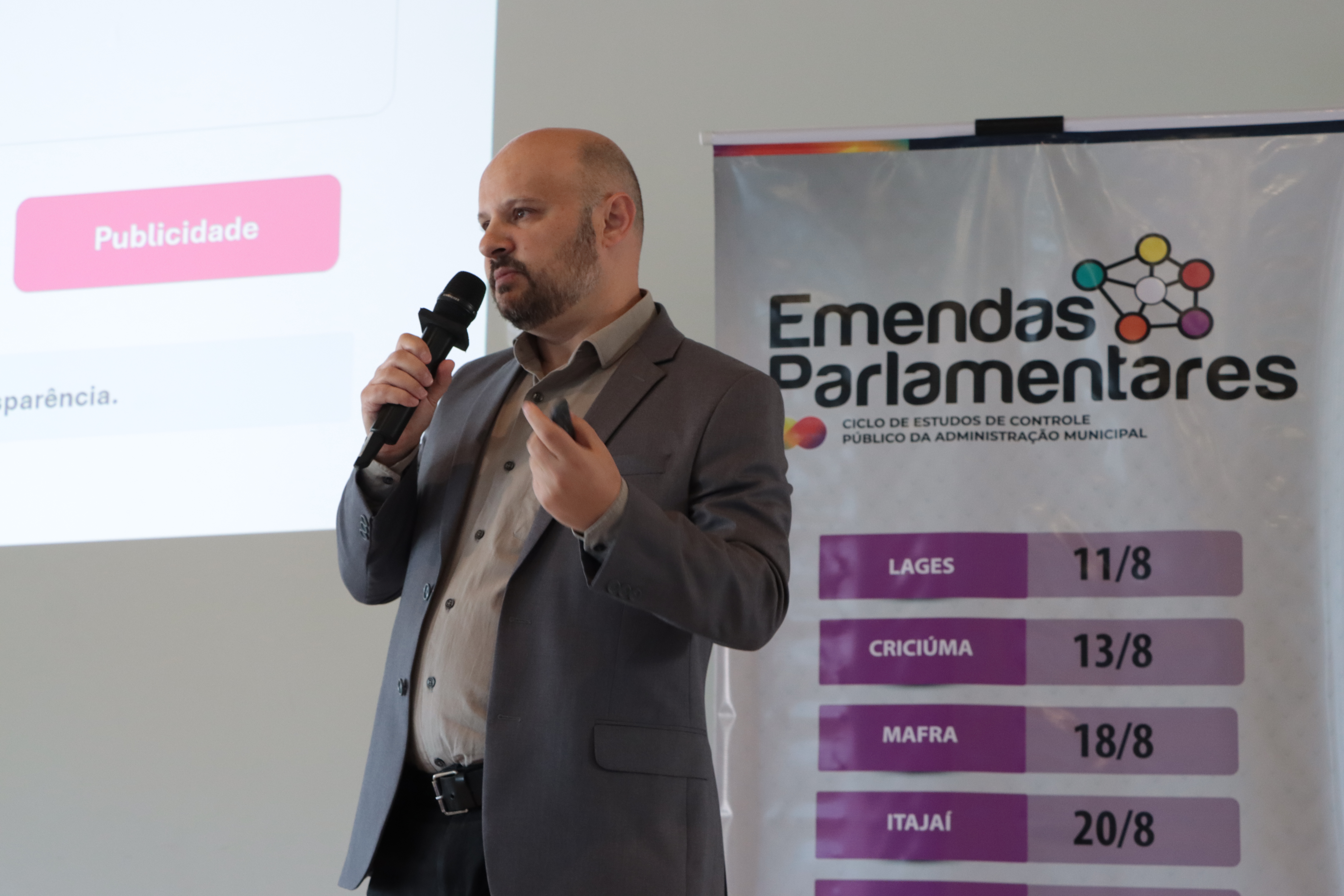 Foto horizontal da apresentação do auditor fiscal de controle externo do TCE/SC, Jean Rodrigo da Silva. Ele está no palco da etapa de Mafra, falando ao microfone.