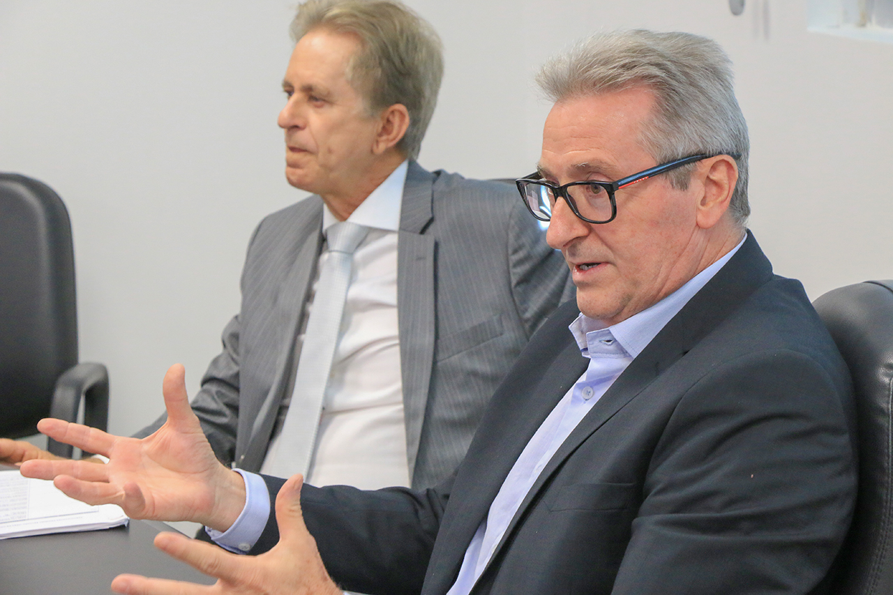 Foto do coordenador da mesa, Neimar Paludo, falando aos demais durante a reunião. Ele é um homem branco, de cabelos grisalhos. Veste paletó preto e usa óculos de grau. Ao seu lado, o conselheiro Luiz Roberto Herbst.  