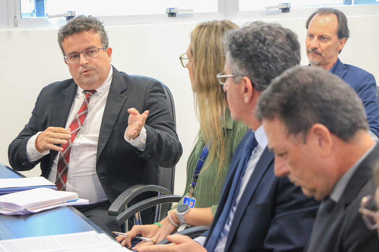 Foto do advogado da Casan Ivan Fischer Júnior falando aos demais durante a reunião. É um homem branco, de cabelos grisalhos. Veste terno e gravata e está ao lado dos outros participantes.