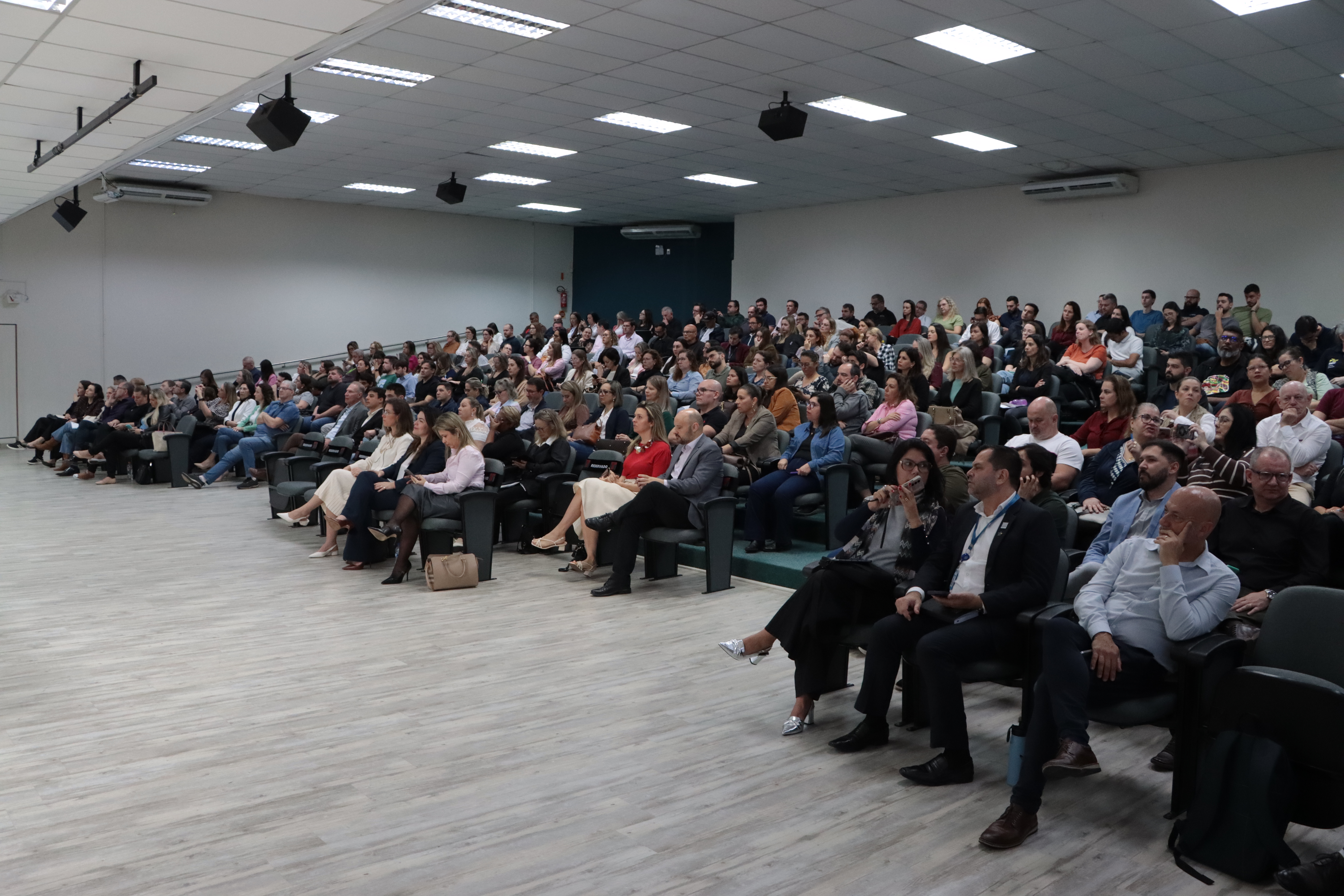 Foto horizontal da plateia do evento. O público ocupa praticamente todos os acentos.