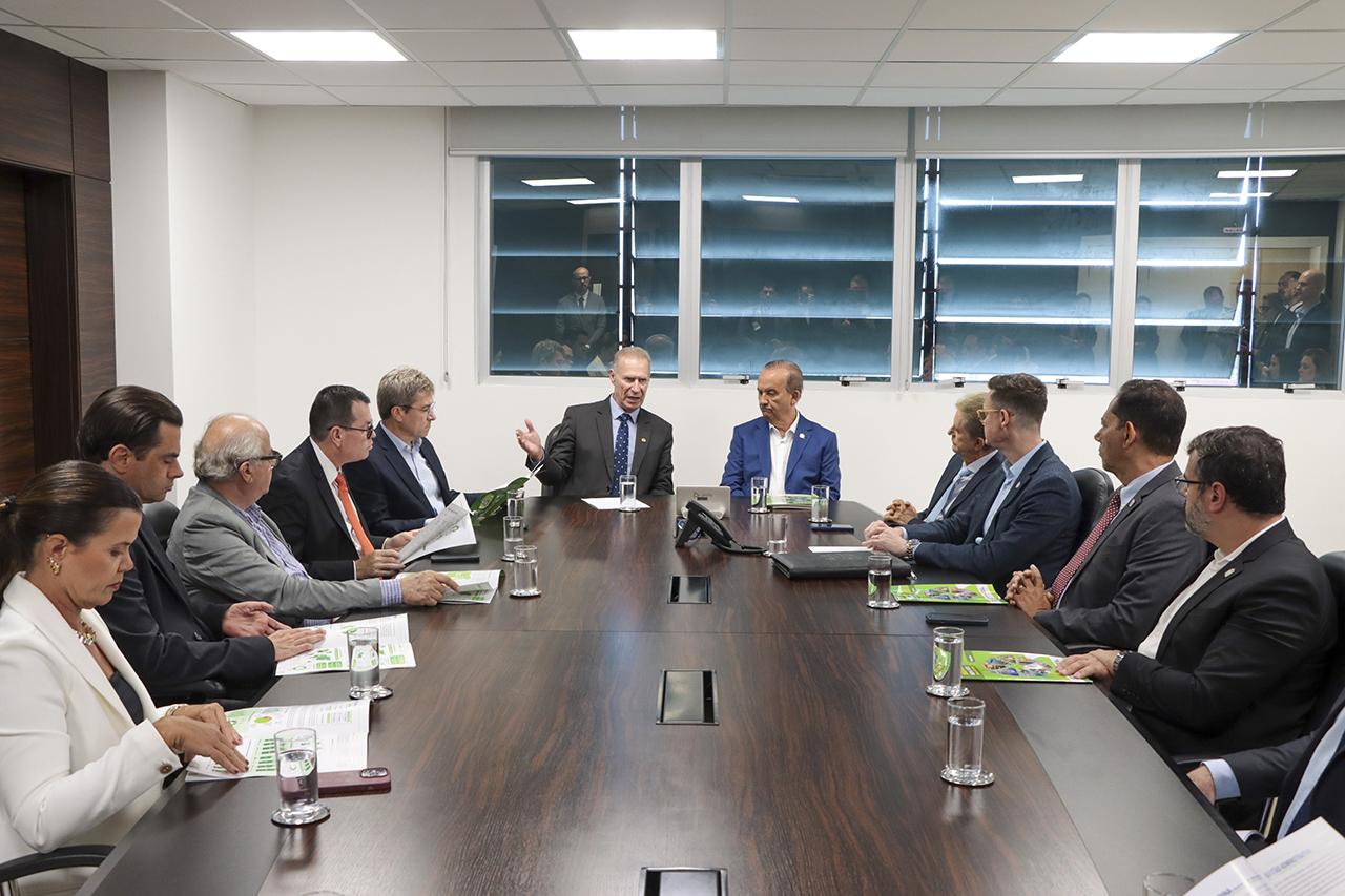 Foto horizontal em ambiente institucional no TCE/SC, mostrando reunião formal durante a entrega das contas do governo de 2025. Ao centro da mesa de reuniões, o presidente do TCE/SC, Herneus De Nadal, e o governador do Estado, Jorginho Mello; ao redor, demais participantes — entre conselheiros, integrantes do governo e representantes do TCE/SC.