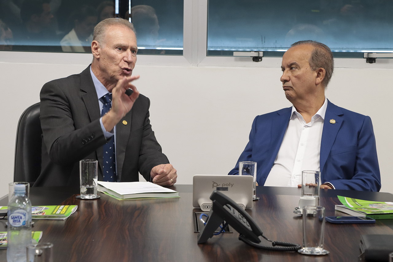 Foto horizontal do presidente do TCE/SC, Herneus De Nadal, falando aos demais durante reunião. É um homem branco, de cabelos claros. Está ao lado do governador do Estado, Jorginho Mello. Ambos sentados diante da mesa de reuniões.