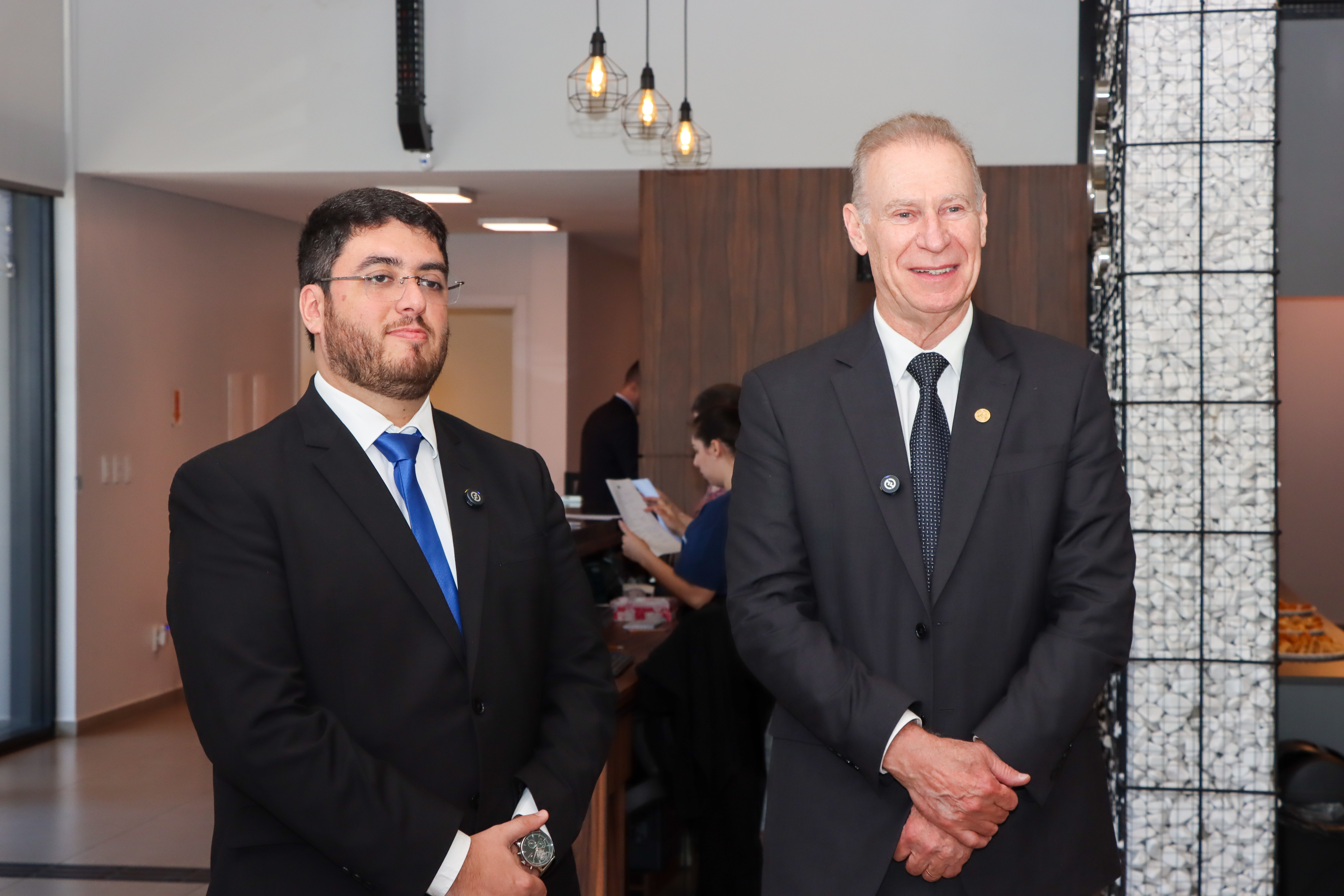 Foto horizontal do presidente Herneus ao lado do presidente da OAB/SC de Chapecó, Guilherme de Oliveira Matos. Eles vestem terno e gravata e estão em pé, sorrindo, em ambiente interno.