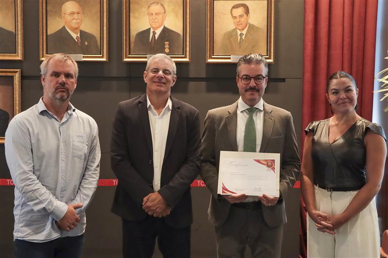 Foto que mostra autoridades lado a lado, durante evento de treinamento, com destaque para o conselheiro Felipe Galvão Puccioni, do TCMRio, ao centro, segurando o certificado referente à capacitação; ao seu lado, o conselheiro substituto Gerson Sicca e a diretora Monique Portella.