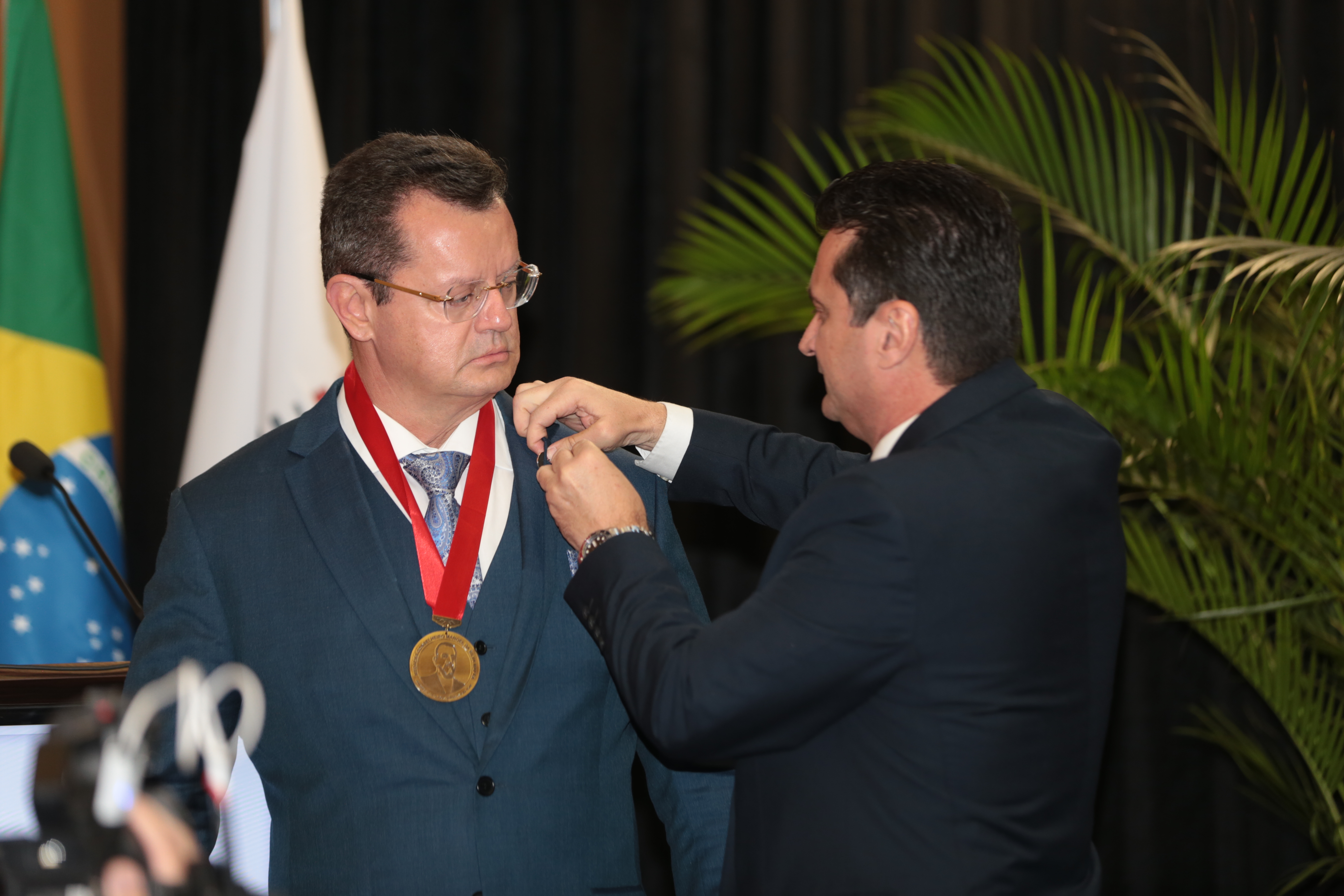 Foto do advogado Claudio Gastão da Rosa Filho, homem branco, de terno azul, com óculos, recebe do presidente do IASC, Gilberto Lopes TEixeira.