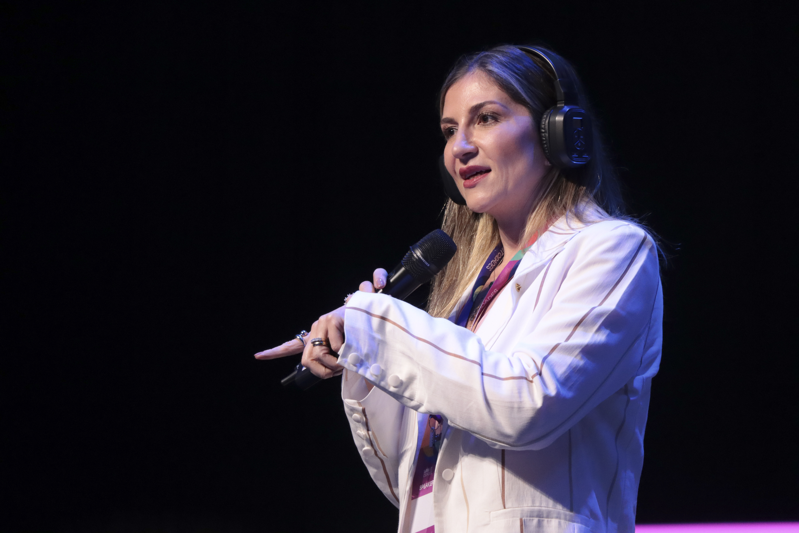 Foto da diretora do Icon, Marina Ferraz de Miranda. Ela usa um blazer branco, está com microfone e fone de ouvido.