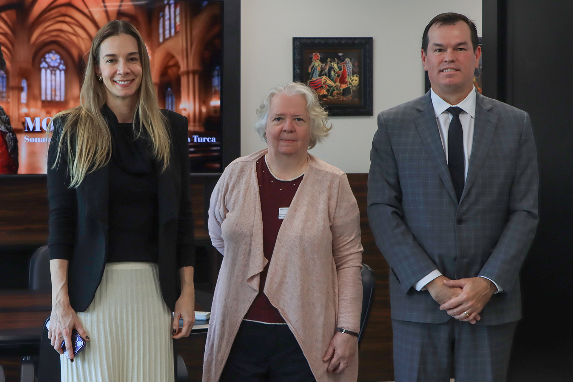 Foto posada do conselheiro Adircélio de Moraes Ferreira Júnior ao lado da bibliotecária Hanne e da servidora Juliana Fritzen, em uma sala do TCE/SC. Ambos sorriem para a foto. 