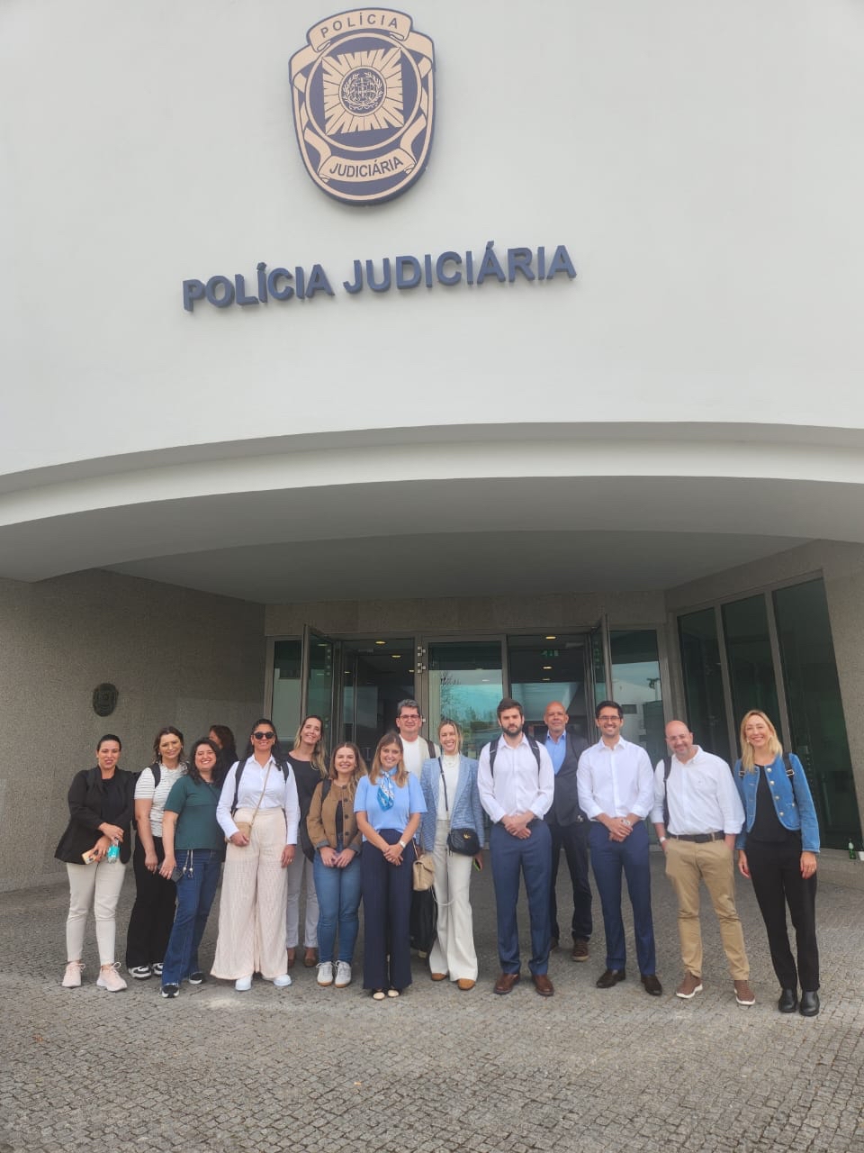 Foto de várias pessoas, lado a lado, em frente ao prédio da Polícia Judiciária, em Portugal. Entre os presentes, os mestrandos da UFSC e os auditores fiscais de Controle Externo Juliano Frasseto Velho, Renato Bossle Miguel e Rafael Scherb. Todos sorriem. 