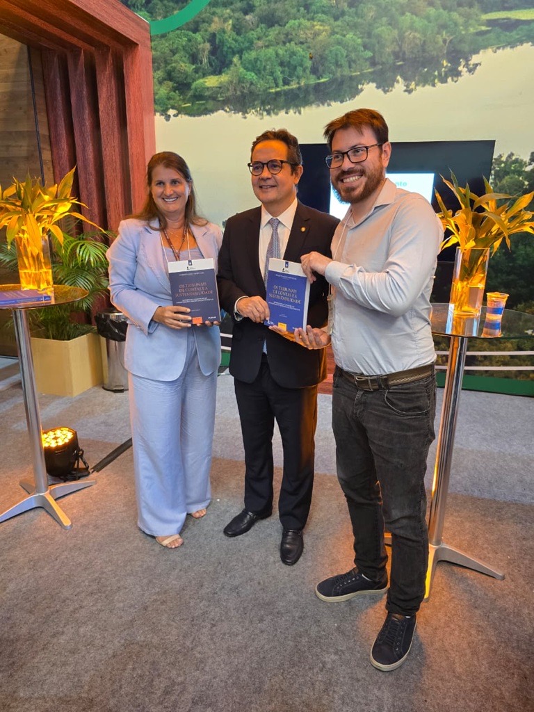 Foto dos autores do artigo e servidores do TCE/SC Elisete Da Correggio e Mateus Galindo ao lado do presidente do IRB. Eles estão em pé, seguram um documento e sorriem para a foto.
