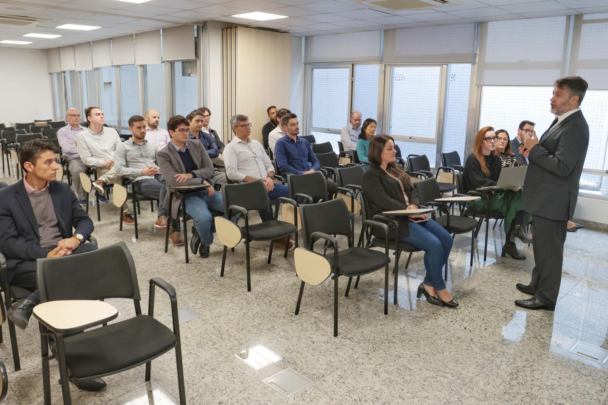 Foto do servidor Rogério Guilherme, à direita, falando à frente de outros membros do TCE/SC, que estão sentados em cadeiras à esquerda da foto, em reunião do Plano de Correição 2023.