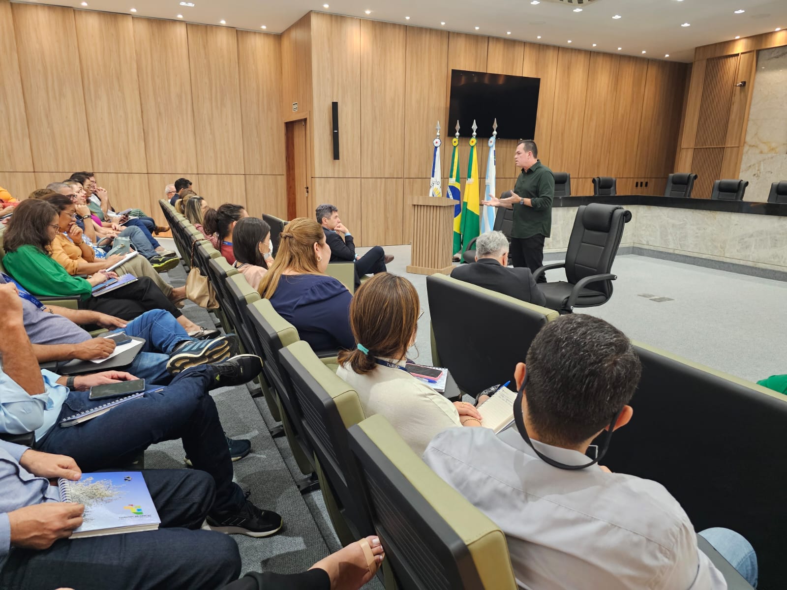 Foto horizontal que mostra o conselheiro Adircélio de Moraes Ferreira Júnior falando aos servidores do TCE/AC. Ele está em pé, no plenário, e os servidores estão sentados em cadeiras, um ao lado do outro. 