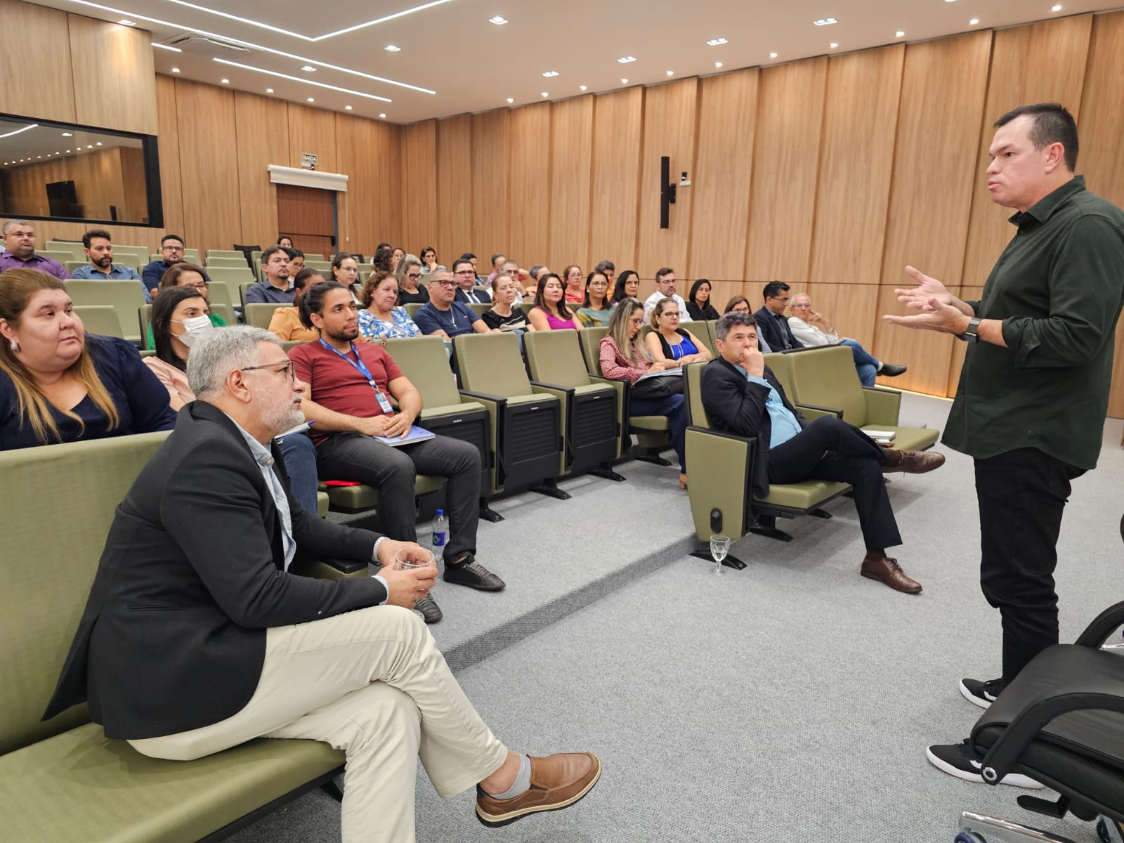 Foto horizontal que mostra o conselheiro Adircélio de Moraes Ferreira Júnior falando aos servidores do TCE/AC. Ele está em pé, no plenário, e os servidores estão sentados em cadeiras, um ao lado do outro. 