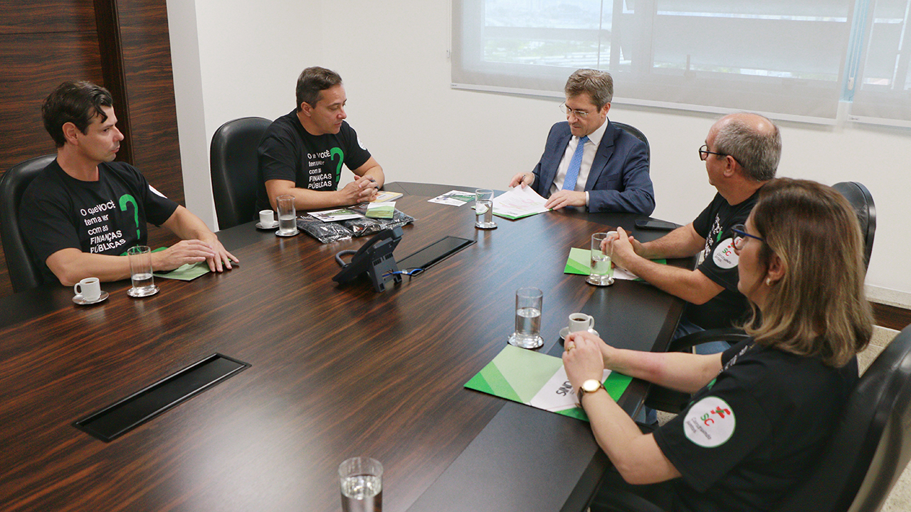 Foto dos participantes da reunião entre o TCE/SC e o Sindaf/SC. Há cinco pessoas sentadas ao redor de uma mesa, enquanto conversam: o conselheiro José Nei Ascari, do TCE/SC, e os membros do Sindaf Pedrinho Pfeifer, André Steffen, Fabiana Corrêa e Sandro Alves. 