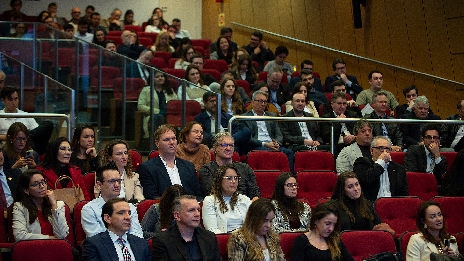 Foto horizontal de parte da plateia participante do Seminário Desenvolvimento e Infraestrutura. Há várias pessoas sentadas em poltronas bordôs, lado a lado, no auditório do TCE/SC. Elas olham para a frente, enquanto assistem a uma das palestras. 