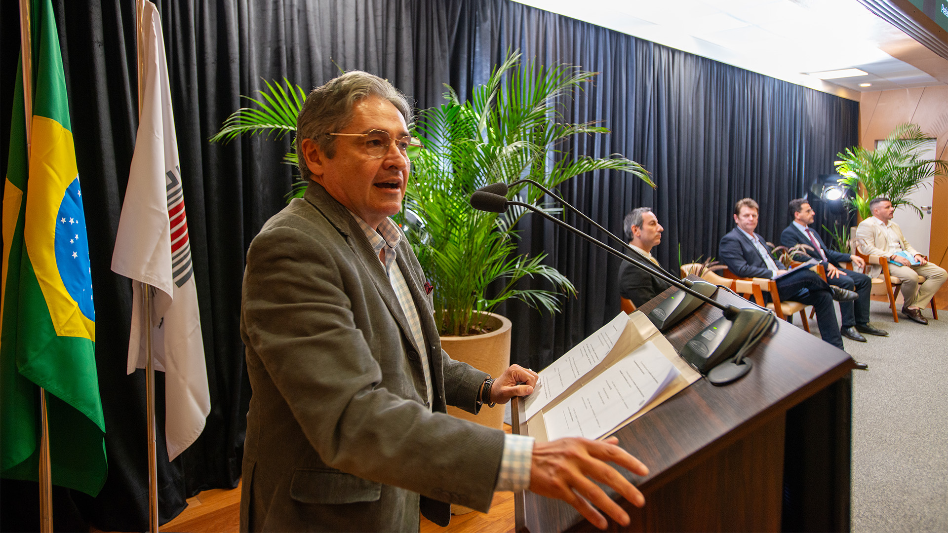 Foto horizontal do conselheiro Aderson Flores discursando no púlpito do auditório do TCE/SC durante o evento. Ele é um homem branco, de cabelos grisalhos. Está em pé, ao lado dos demais integrantes da mesa de discussões sobre regionalização. Entre os presentes, Ramiro Zinder, Onésimo José Sell, Diogo Pinheiro e Estêner Soratto. 