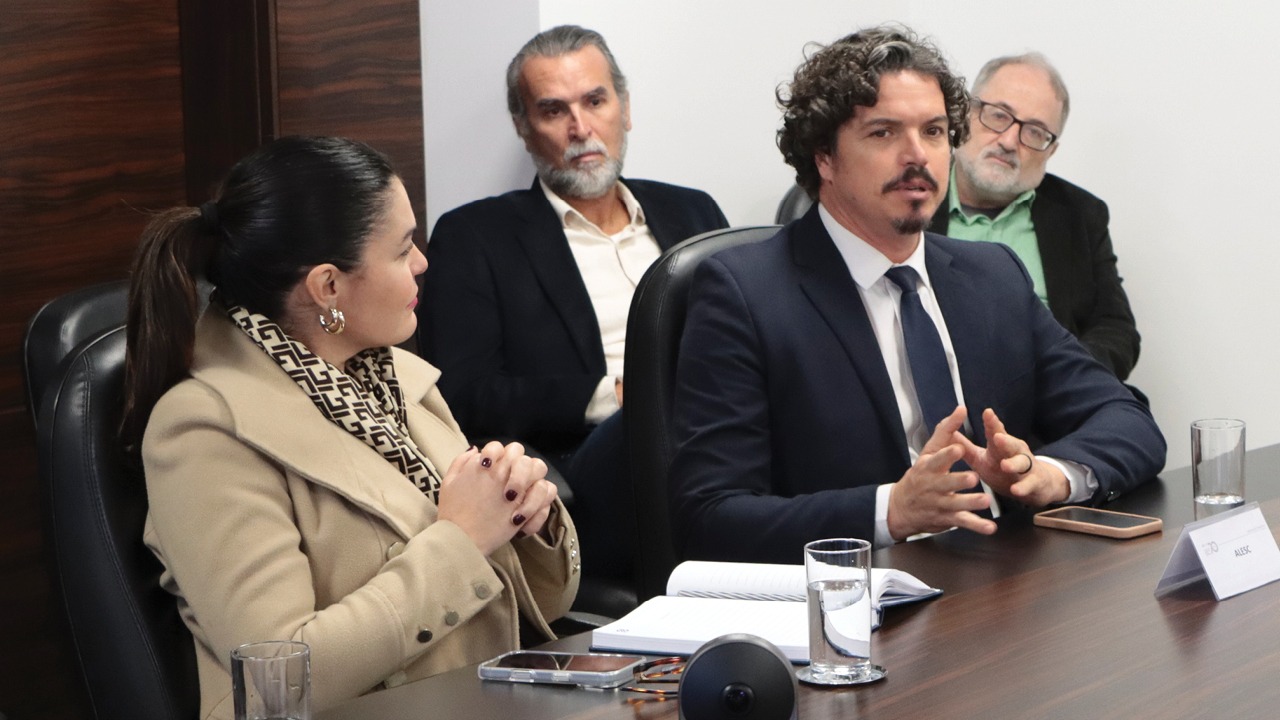Foto horizontal que mostra o deputado estadual Marquito falando aos demais durante a reunião. Ao seu lado, a diretora Monique Portella e outros integrantes da reunião. 