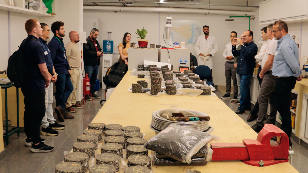 Foto horizontal que mostra a equipe da Amurel em visita ao Laboratório do TCE. Ao centro, na mesa, várias amostras de asfalto coletadas.