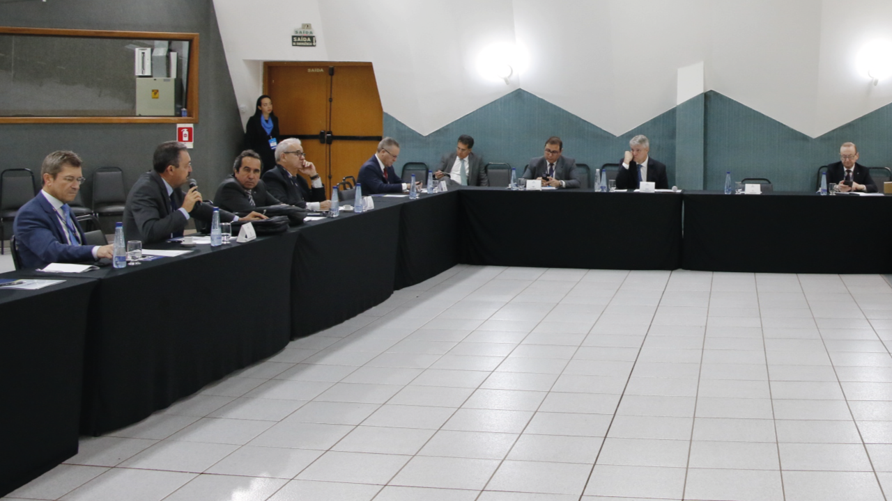 Foto da reunião do CNPTC. Diversas pessoas estão sentadas em volta de mesas, entre elas, o conselheiro José Nei Ascari, que está no lado esquerdo da foto, em primeiro plano.
