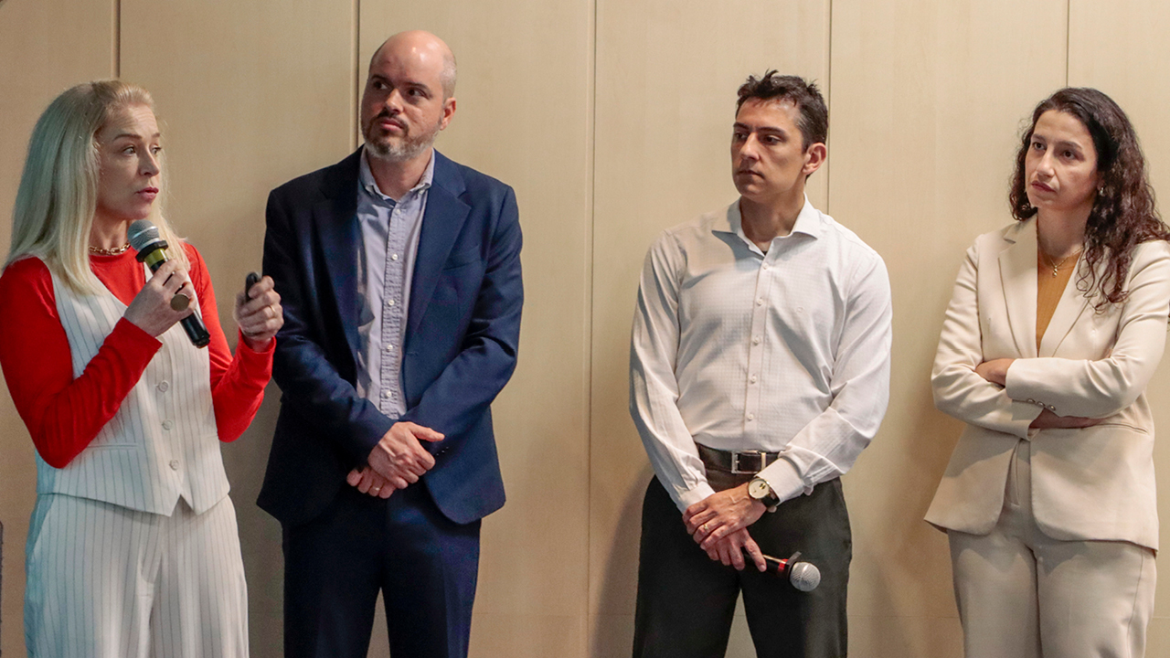 Foto horizontal de quatro servidores no evento. Pela ordem, da direita para a esquerda,  assessora técnica da DTI, Janaina Siqueira, diretor da DTI, Rafael Queiroz Gonçalves; coordenador do setor de banco de dados, Alexandre Matos; e a assessora de TI responsável técnica pelo projeto, Cristina Bona.