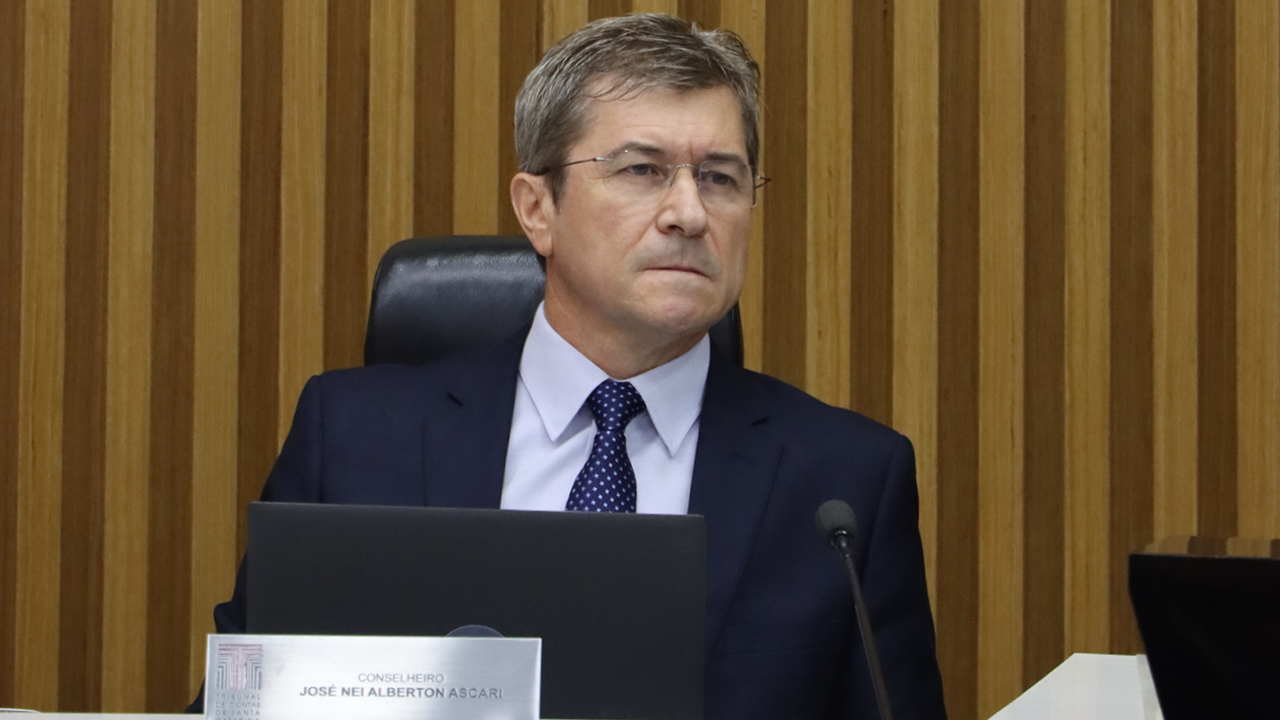 Foto horizontal do vice-presidente do TCE/SC, conselheiro José Nei Ascari, durante sessão. É um homem branco, de cabelos claros. Veste terno e gravata e usa óculos de grau. Com a expressão séria, está sentado diante da bancada circular no Plenário. 