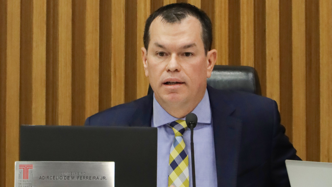 Foto do conselheiro Adircélio de Moraes Ferreira Júnior falando ao microfone durante a sessão. É um homem branco, de cabelos escuros. Veste terno e gravata e está sentado diante da bancada circular no Plenário.