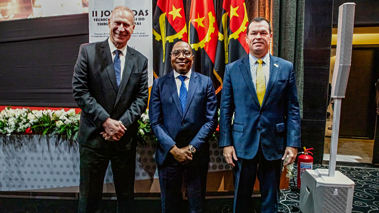 Foto do presidente do TCE/SC, Herneus de Nadal, do presidente do TCE de Angola e do conselheiro Adircélio, no palco do auditório onde ocorreu o evento.