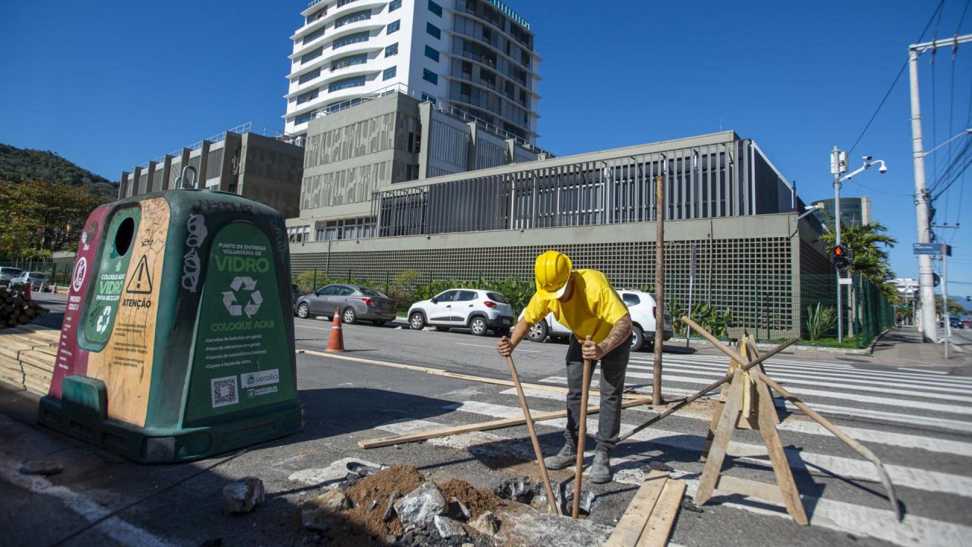 Banner horizontal com foto de um trabalhador realizando suas atividades de manutenção de uma rua, em frente ao TCE/SC, um prédio de 13 andares de vidro espelhado. Ele veste uniforme amarelo e equipamentos de segurança. 