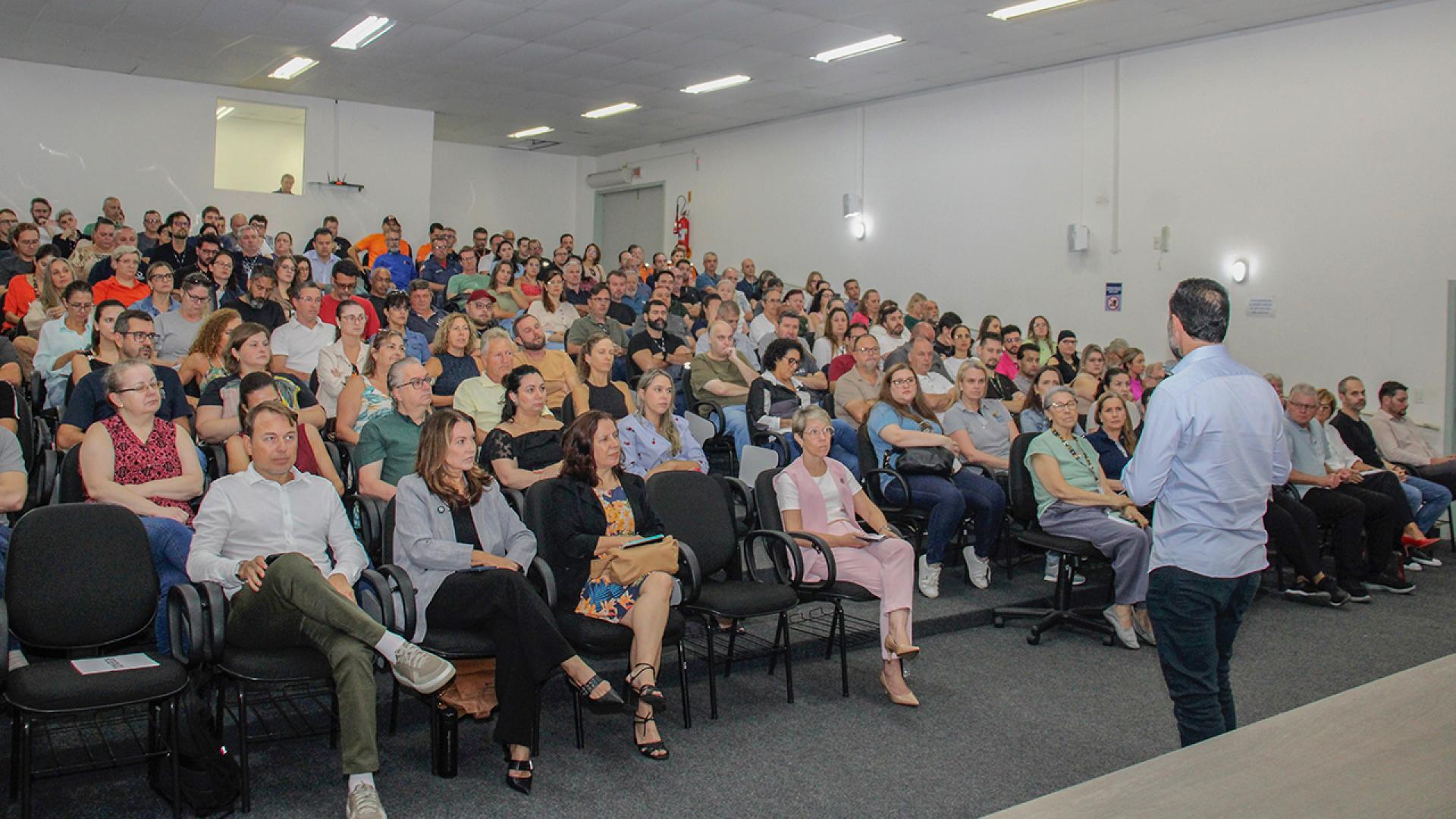 Banner horizontal com foto de palestra realizada em auditório. À frente, servidor da CGU fala ao público, em pé, em frente ao palco. Na primeira fila, estão os servidores do TCE/SC Luiz Alexandre Steinbach e Caroline Souza. Nas poltronas, os participantes, atentos à fala. 