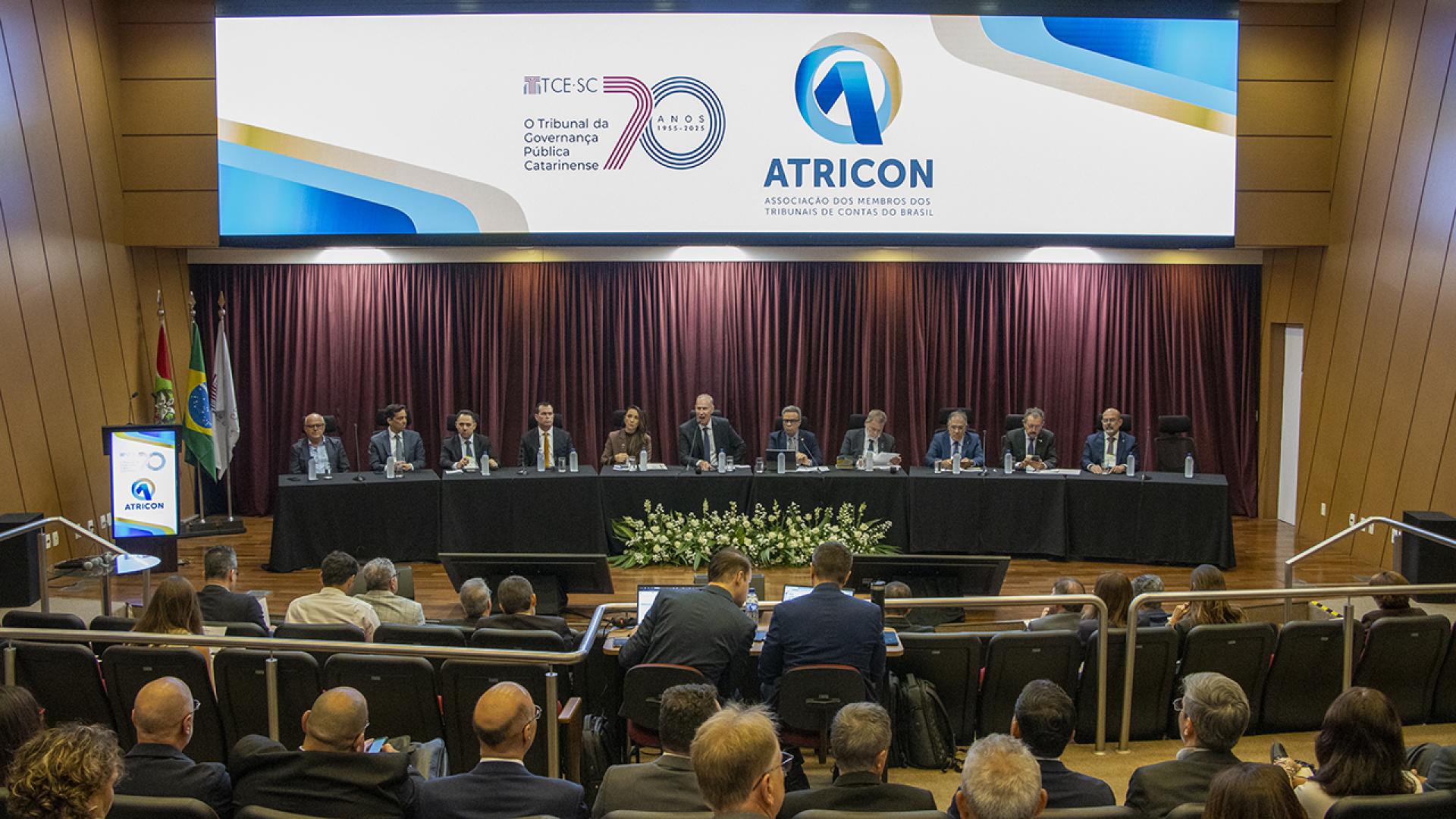 Foto horizontal do auditório bordô do TCE/SC. Na mesa, 10 conselheiros e 1 conselheira. Ao centro, o presidente do TCE/SC,  Herneus De Nadal e ao lado dele o presidente da Atricon Edilson Silva. 