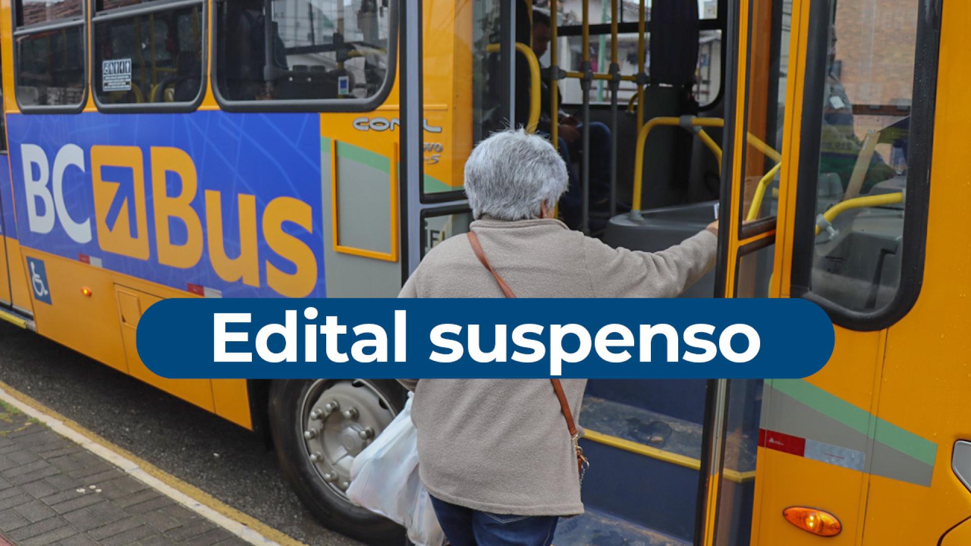 Imagem tem como fundo um ôninus amarelo escrito BC Bus na lateral. Há uma mulher de cabelo grisalho entrando pela porta da frente. Ao centro está escrito Edital Suspenso, em letras brancas sobre uma tarja azul. 