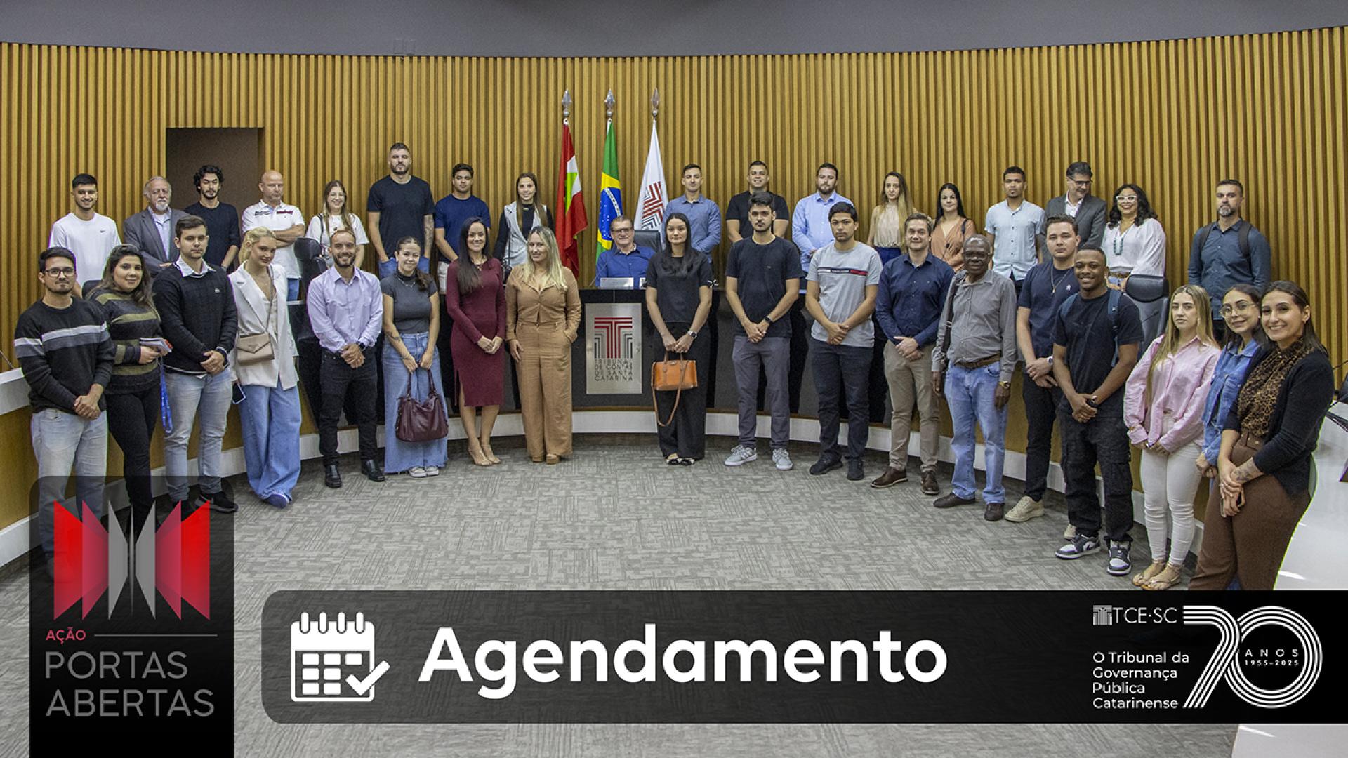 Banner horizontal com foto de um grupo de estudantes e adultos reunidos no plenário do Tribunal de Contas de Santa Catarina durante visita institucional. As pessoas estão posicionadas em semicírculo diante da mesa principal do plenário, com bandeiras ao fundo e o brasão do TCE/SC ao centro. Na parte inferior da imagem aparece uma faixa escura com o texto “Agendamento” e um ícone de calendário. À esquerda, está o logotipo do programa Ação Portas Abertas e, à direita, logo do TCE/SC.