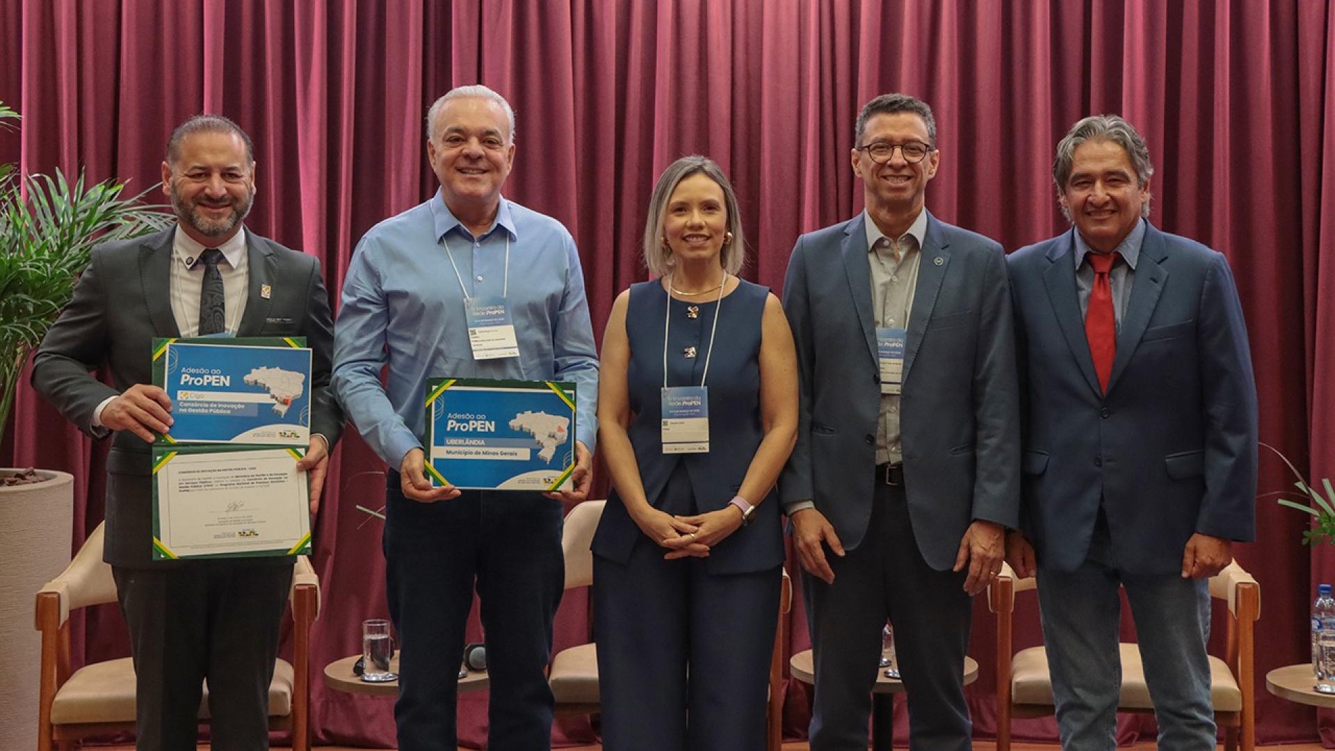 Banner horizontal com foto de cinco pessoas em pé, lado a lado, no auditório do TCE/SC, durante o encontro da Rede ProPEN. Dois homens seguram certificados de adesão à rede e os mostram para a foto. À direita, entre os presentes, está o conselheiro do TCE/SC Aderson Flores. 