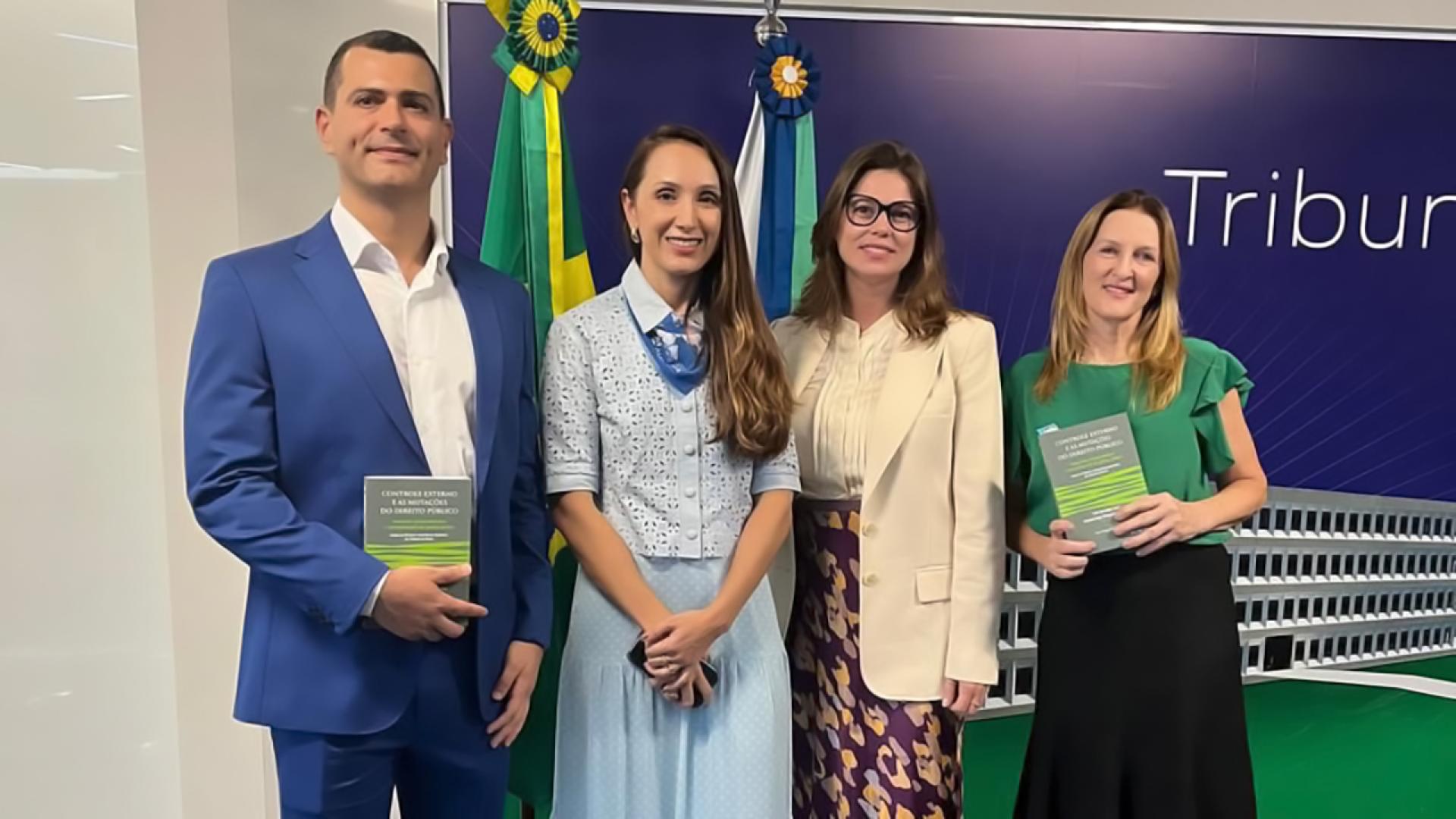 Banner horizontal com foto de quatro pessoas em pé, uma ao lado da outra. São elas: a conselheira substituta Sabrina Nunes Iocken e os servidores Sonia de Oliveira (de blusa verde) e Rafael Galvão, ao lado de Milene Cunha (de azul). Ambos sorriem.
