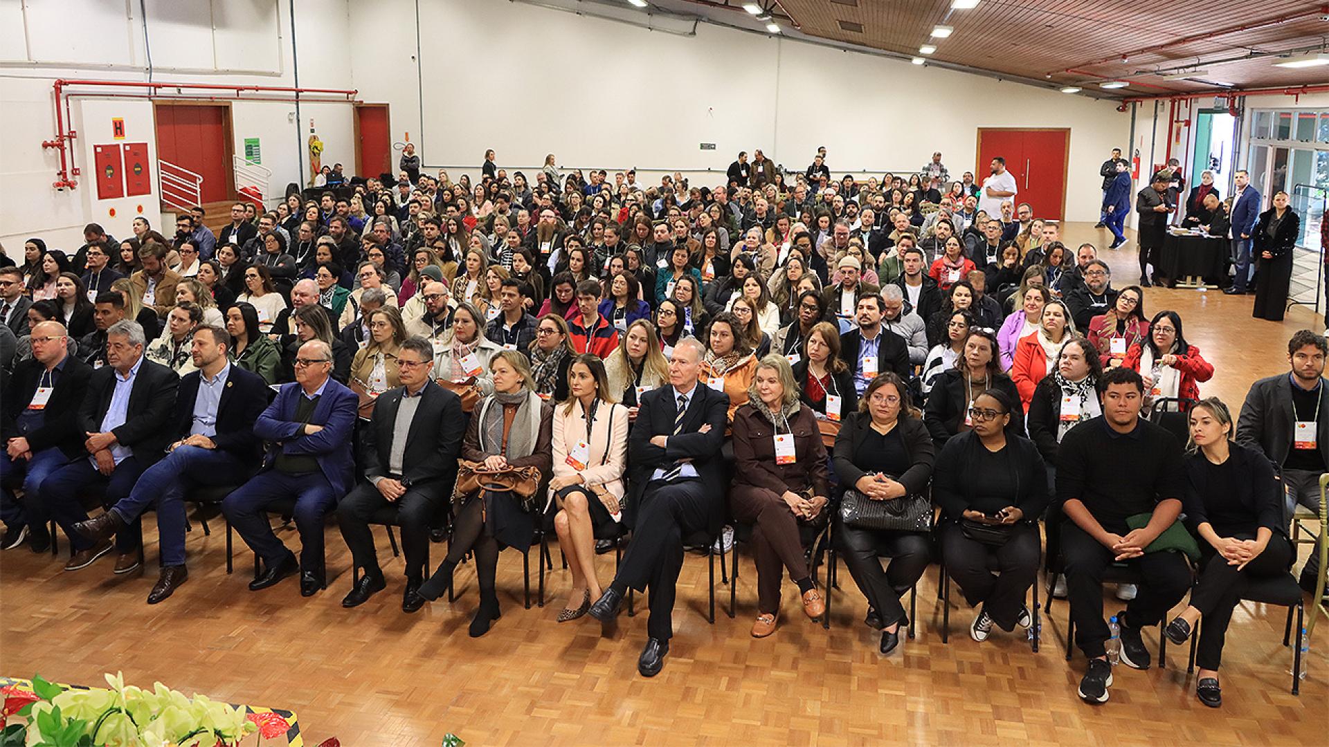 Imagem mostra cerca de 300 pessoas sentadas em um auditório. Elas estão de frente para o observador.