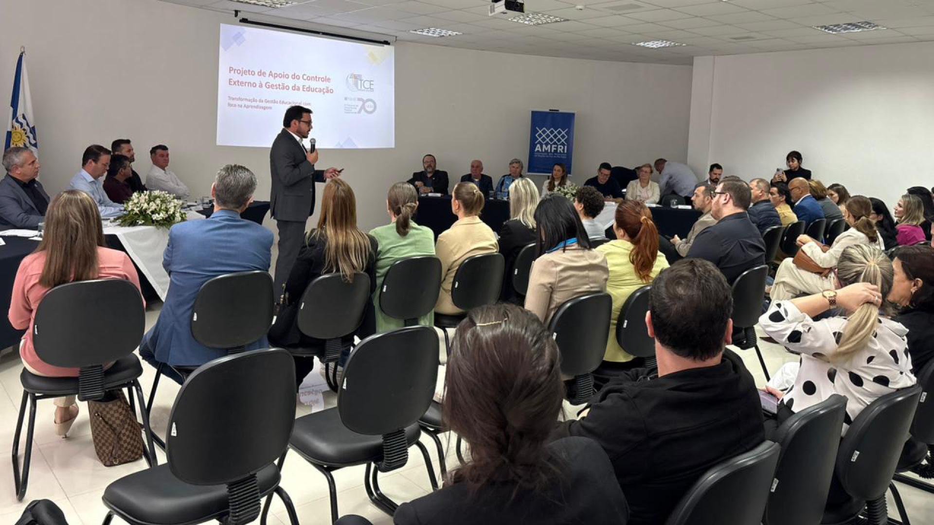 Imagem mostra um grupo de pessoas observando, ao fundo, uma explanação de um homem que está em pé.