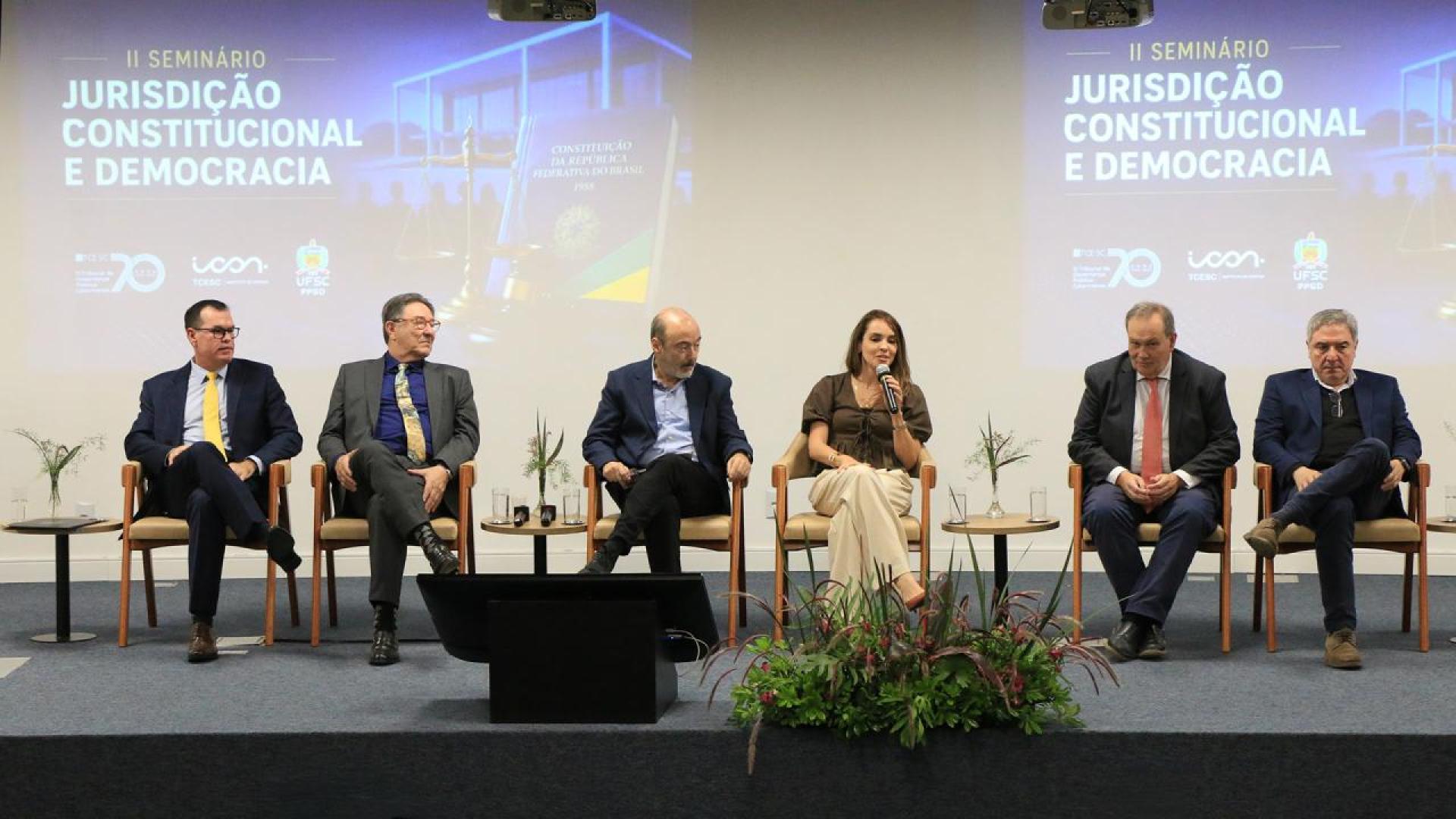 Banner horizontal com foto de seis autoridades sentadas em poltronas lado a lado no palco do auditório do TCE/SC. Entre os presentes, o corregedor-geral, conselheiro Adircélio Ferreira Júnior, e o professor Luiz Henrique Cademartori. O cenário tem plantas decorativas. Ao fundo, projeção de slides.