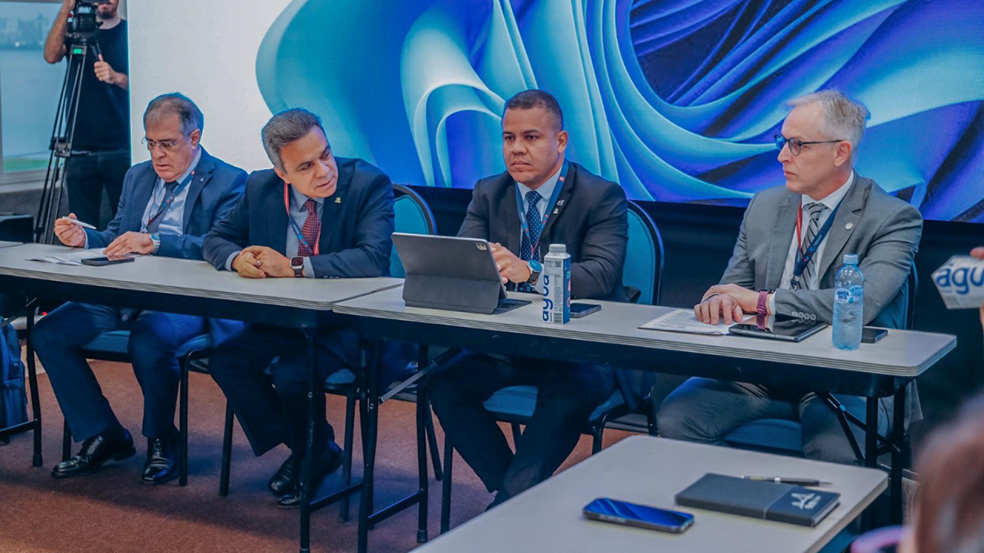 Foto horizontal de quatro homens sentados diante de uma mesa, lado a lado, durante reunião. Entre os presentes, o diretor-geral de Controle Externo do TCE/SC, Sidney Tavares, e o presidente da Atricon, conselheiro Edilson Silva. Todos vestem terno e gravata. O fundo mostra imagem azul abstrata.
