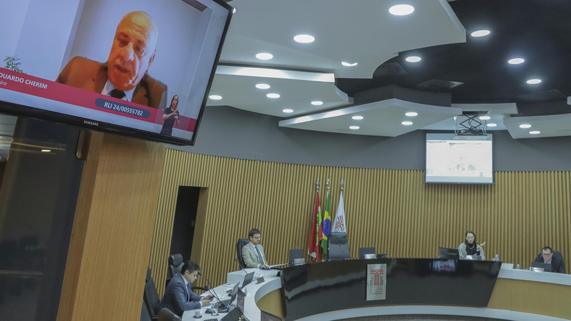    Banner horizontal com foto dos integrantes da Segunda Câmara no Plenário do TCE/SC.  Ao redor da bancada circular do Plenário, entre os presentes, os conselheiros Adircélio de Moraes Ferreira Júnior e conselheiro substituto Céber Muniz Gavi, e o procurador Sérgio Ramos. Os conselheiros Luiz Eduardo Cherem aparece no monitor. 